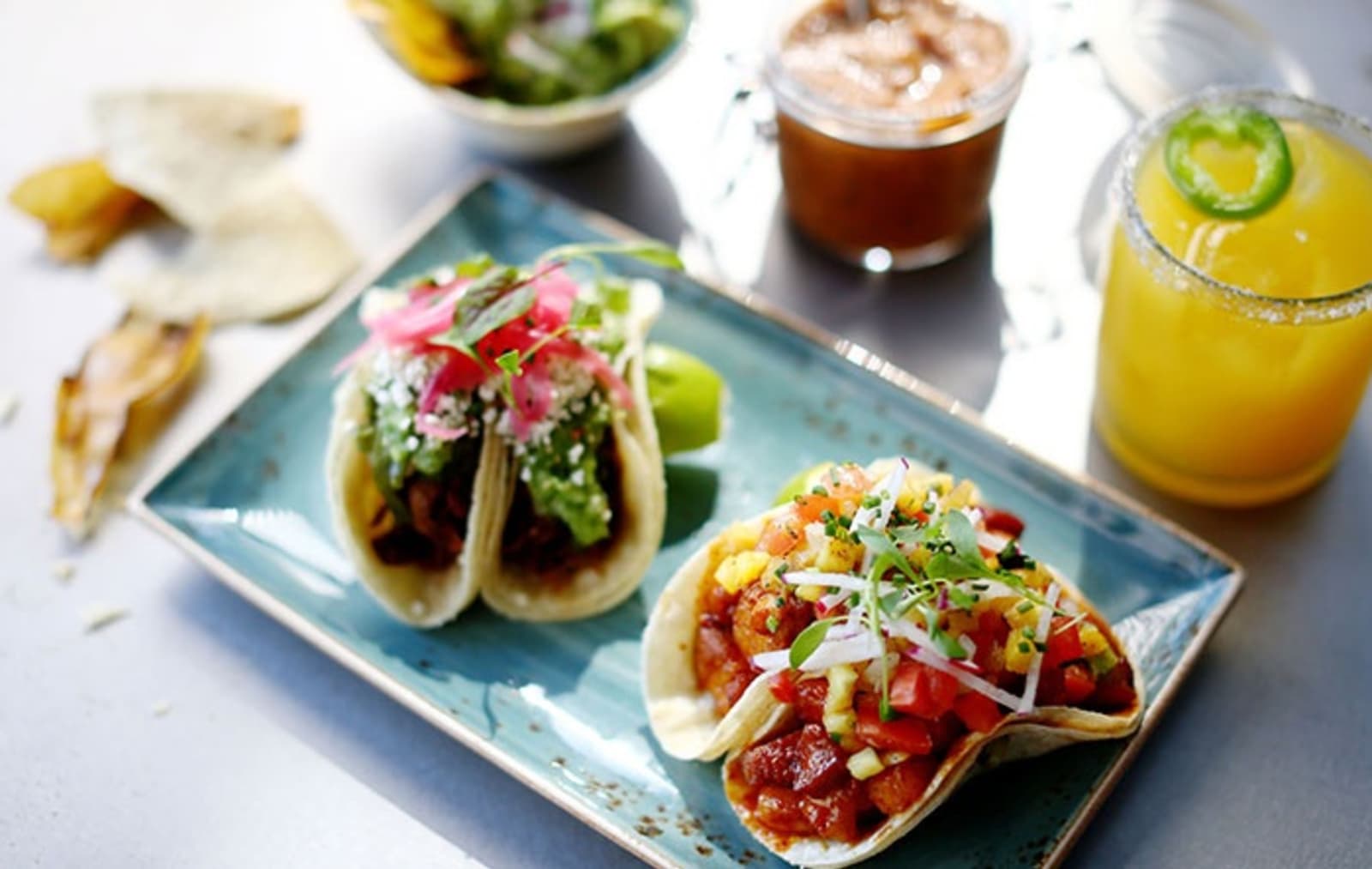 Tacos served on a plate with a dip and drink in the background
