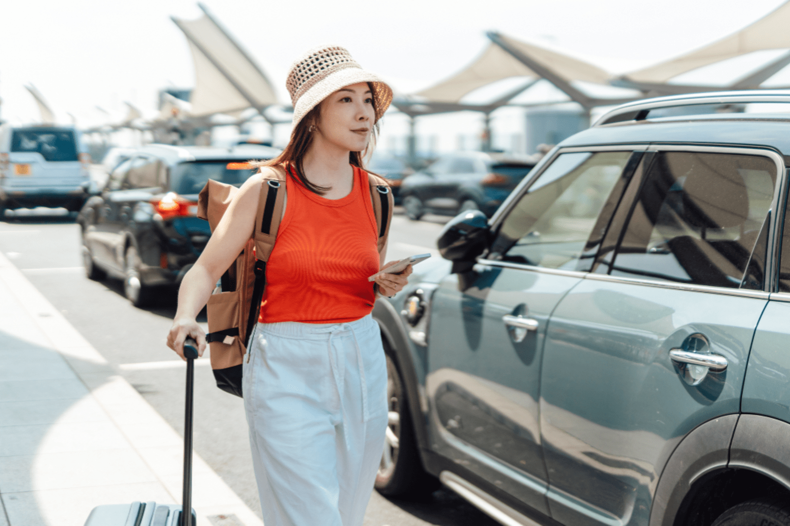 A woman outside a busy airport waiting for her ride share to arrive