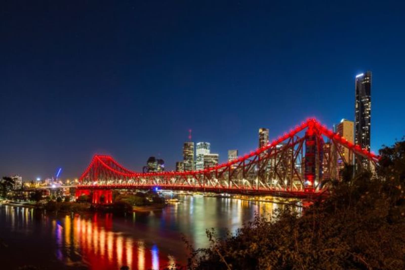 Brisbane cross the river bridge lite up red with city view in background during nighttime