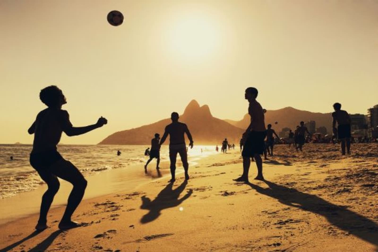 People playing soccer on a beach during sunset