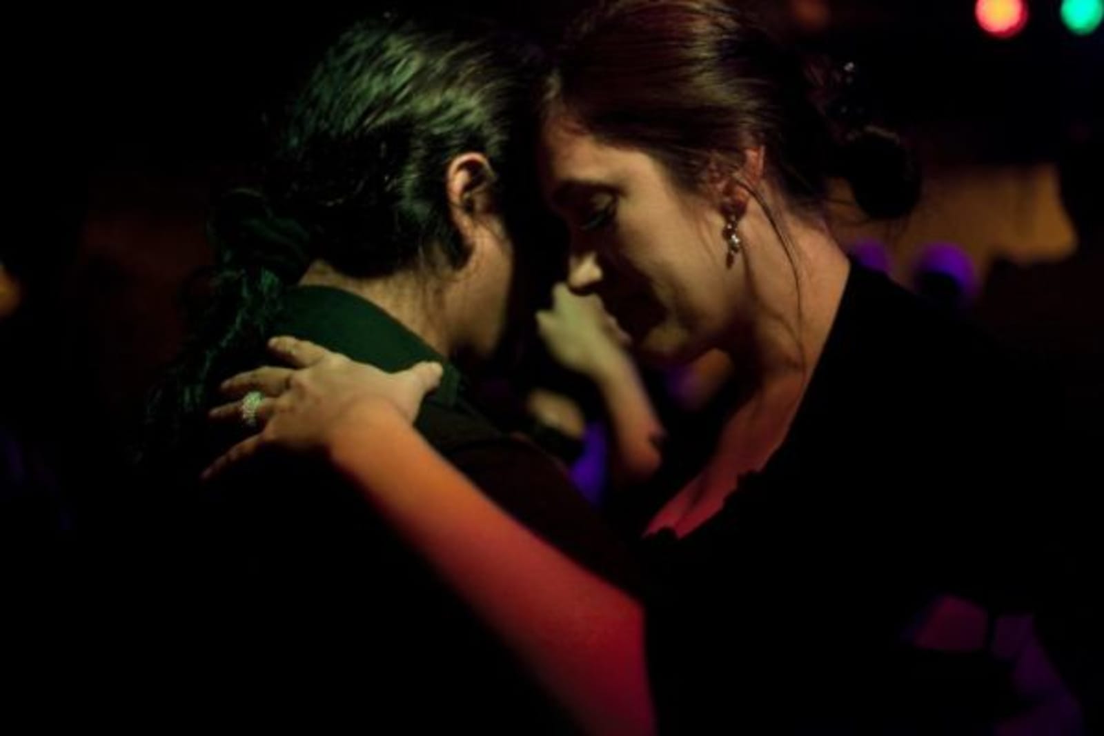 Male and female dancing in dark room, spots of coloured light hitting their faces