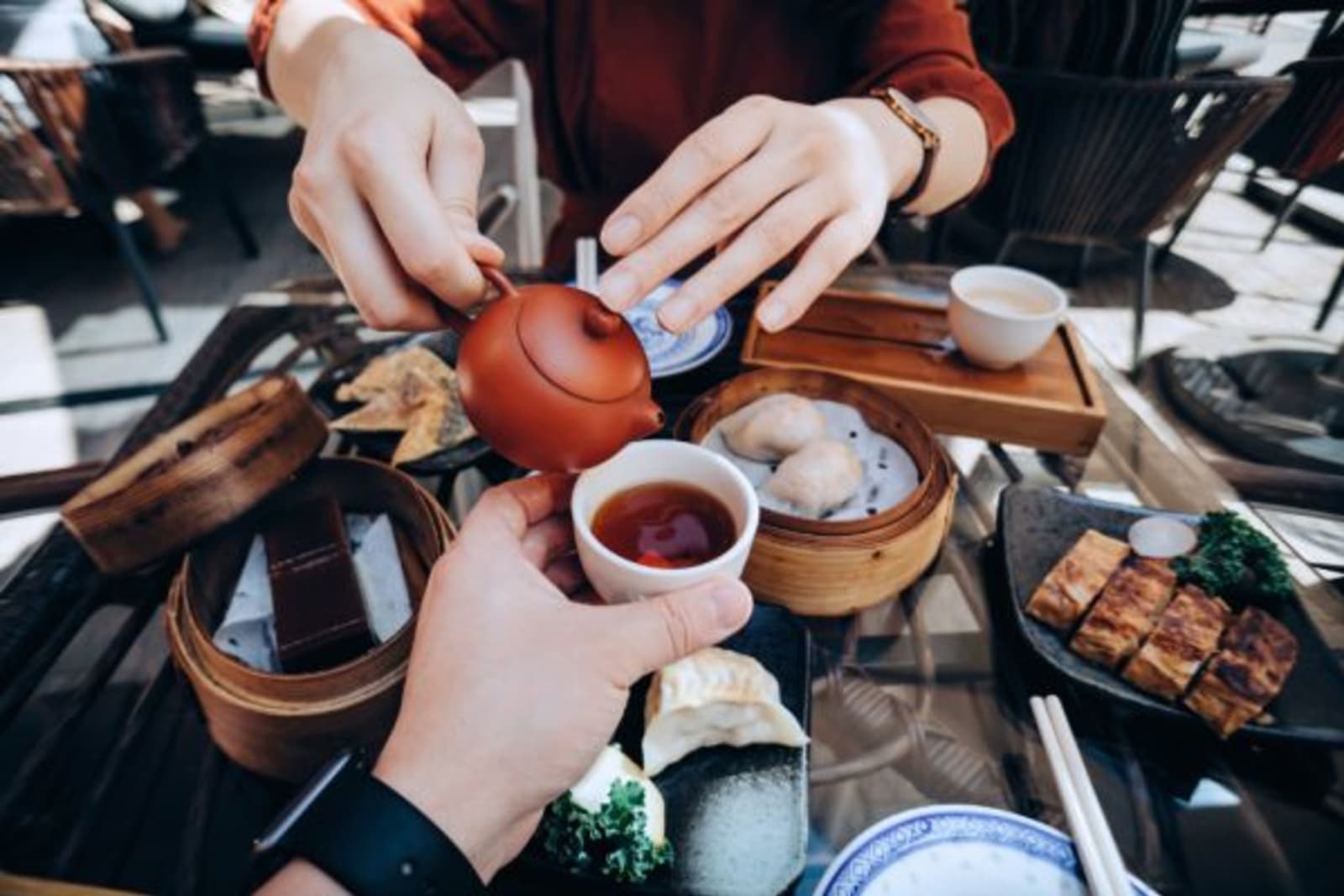 Woman pouring tea in a cup for a man and a table that has dumplings and traditional Asian foods