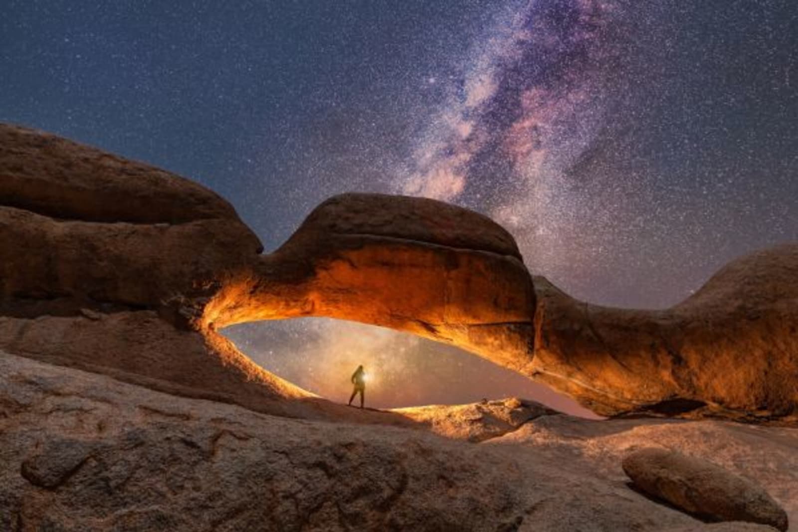 Person with torch standing under a rock arc, sky is full of stars