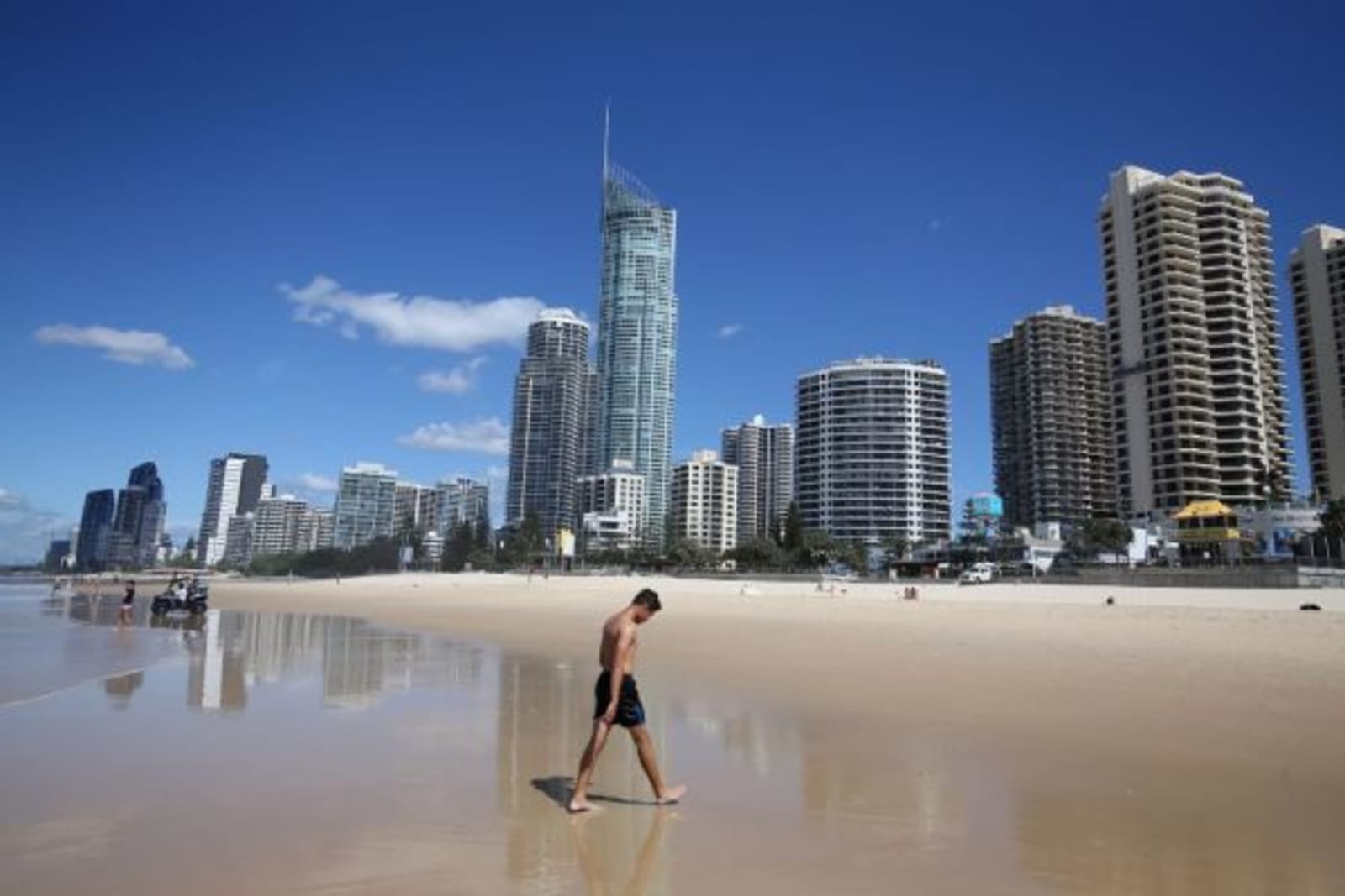 Man walking out of the surf towards beach and skyscrapers