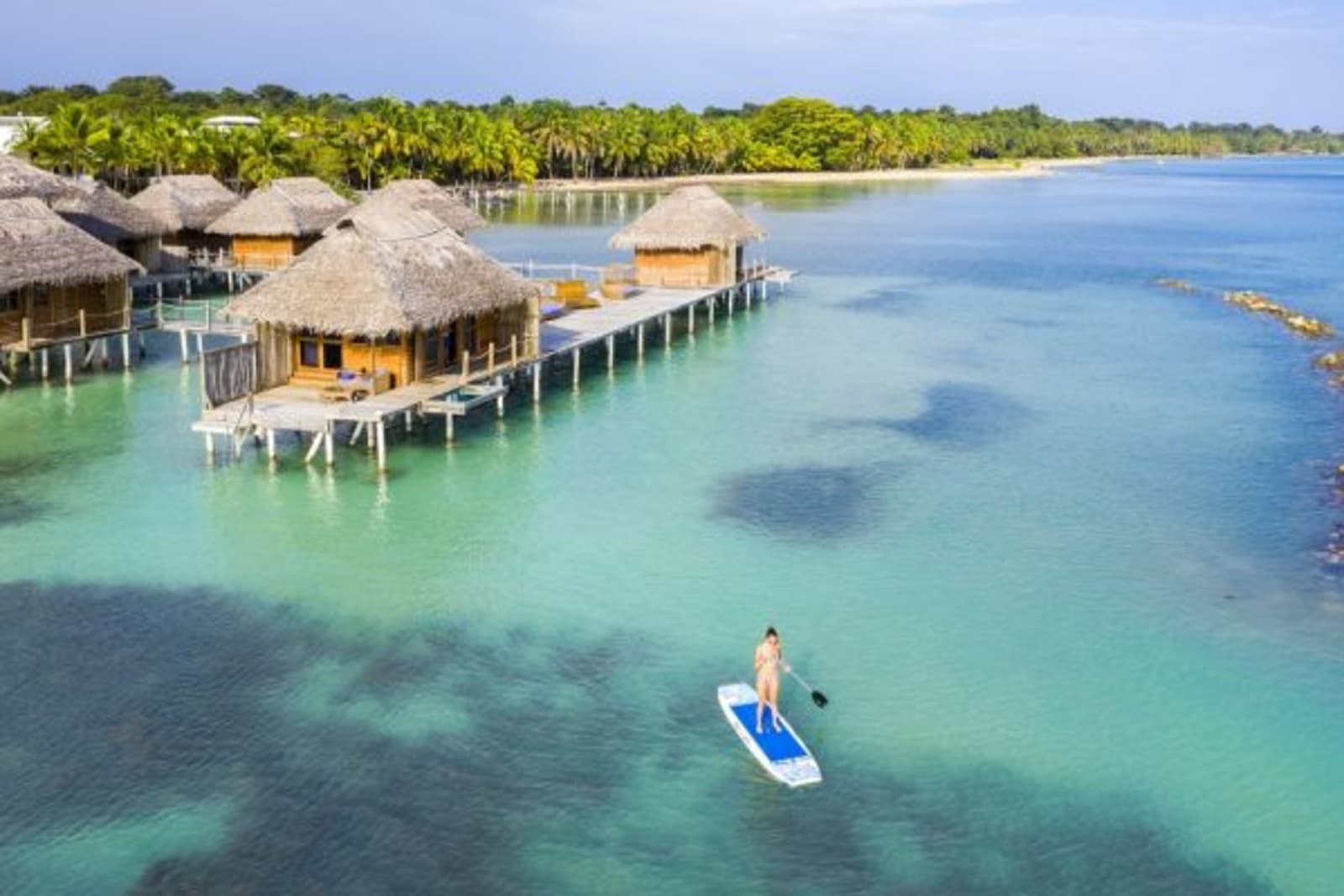 Woman paddle boarding in clear water next to floating resort