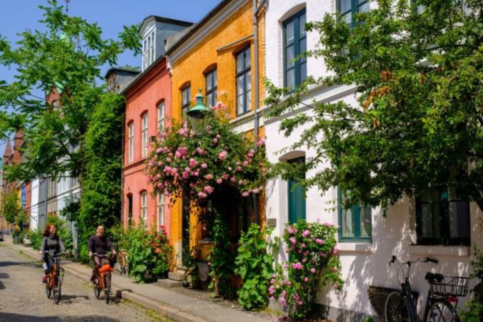 Couple cycling past colourful buildings and greenery