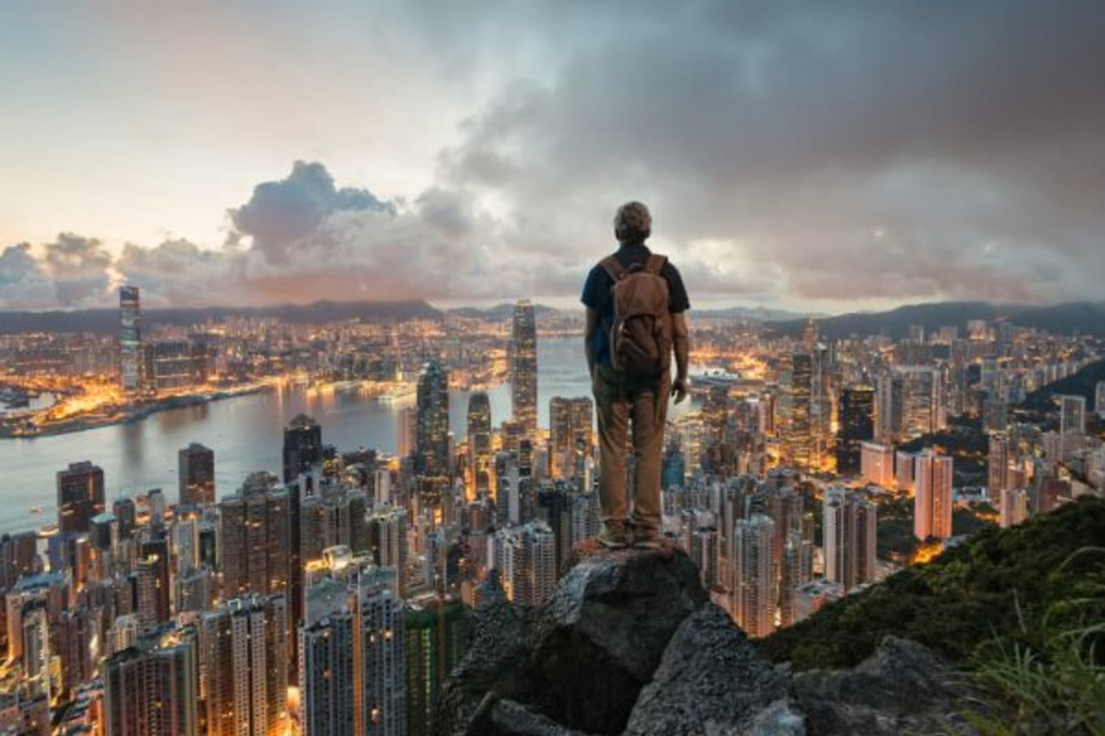 Man standing on edge of a mountain on a rock looking at Hong Kong city light up