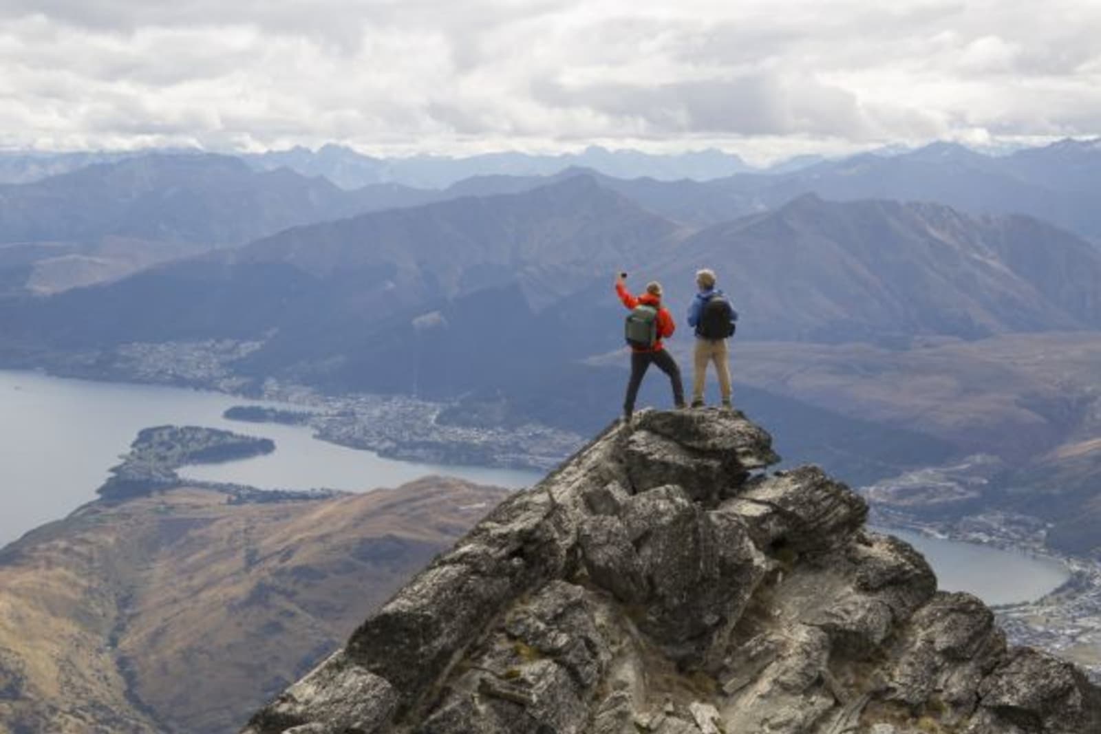 Distant shot of two hikers taking a selfie on top of a mountain in Queenstown