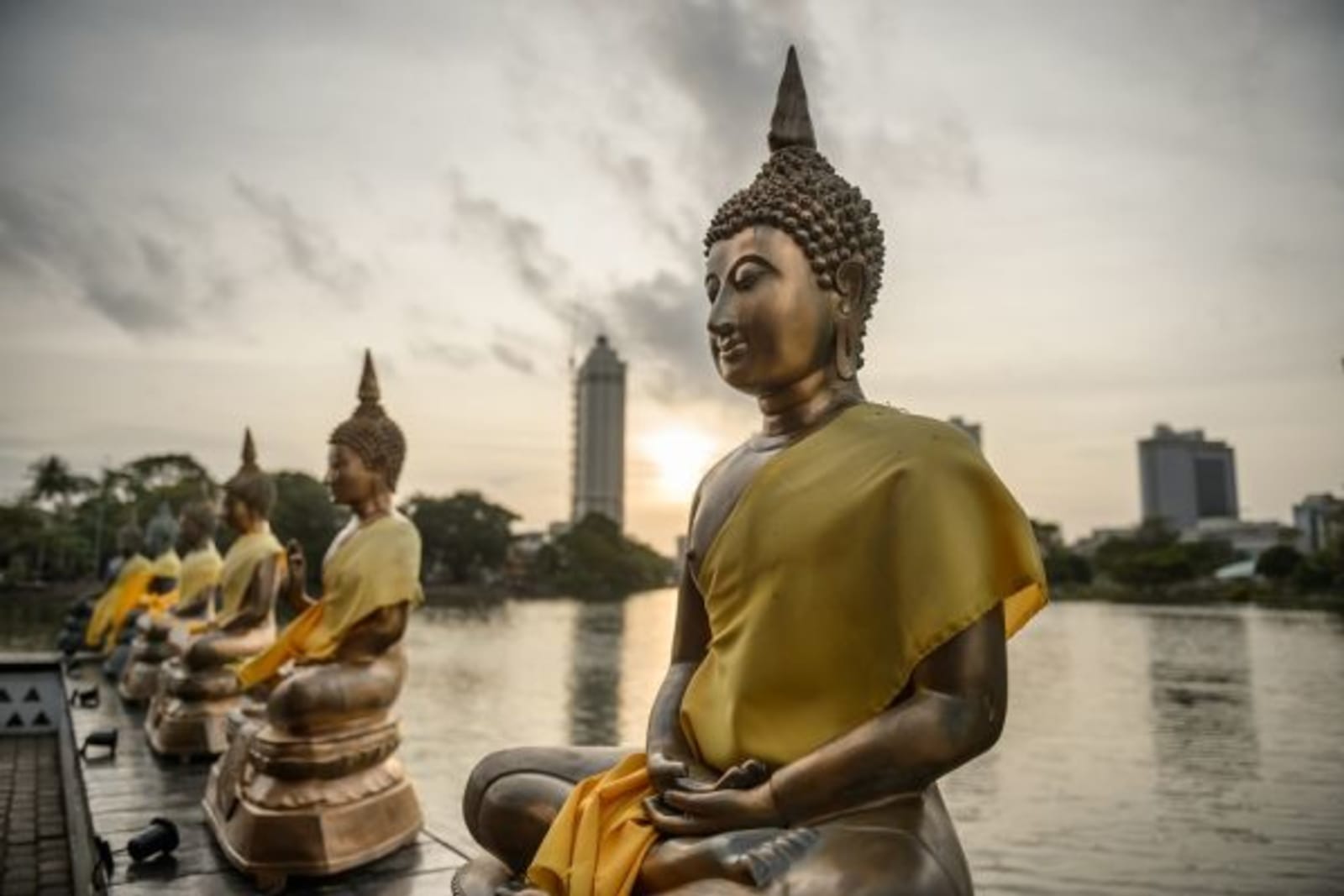 Row of statue Buddhist sat on a bridge overlooking a lake and temple