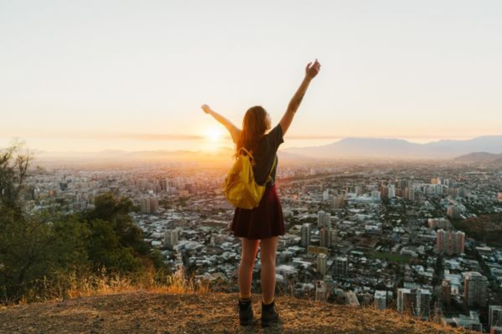 Female throwing her hands up in the air at a lookout of a city during sunset