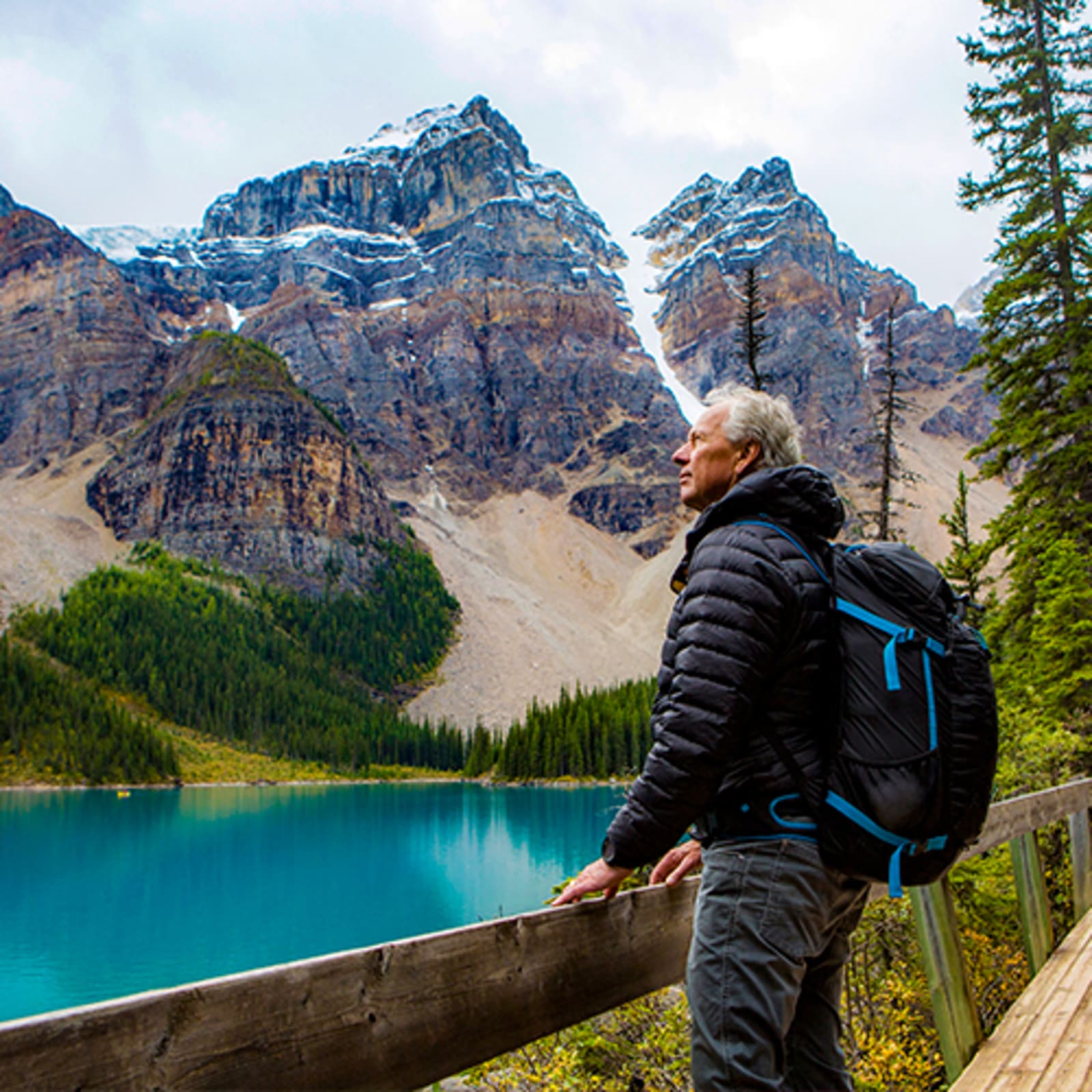 Man looking out at tall, snow covered hills across from a bright blue lake