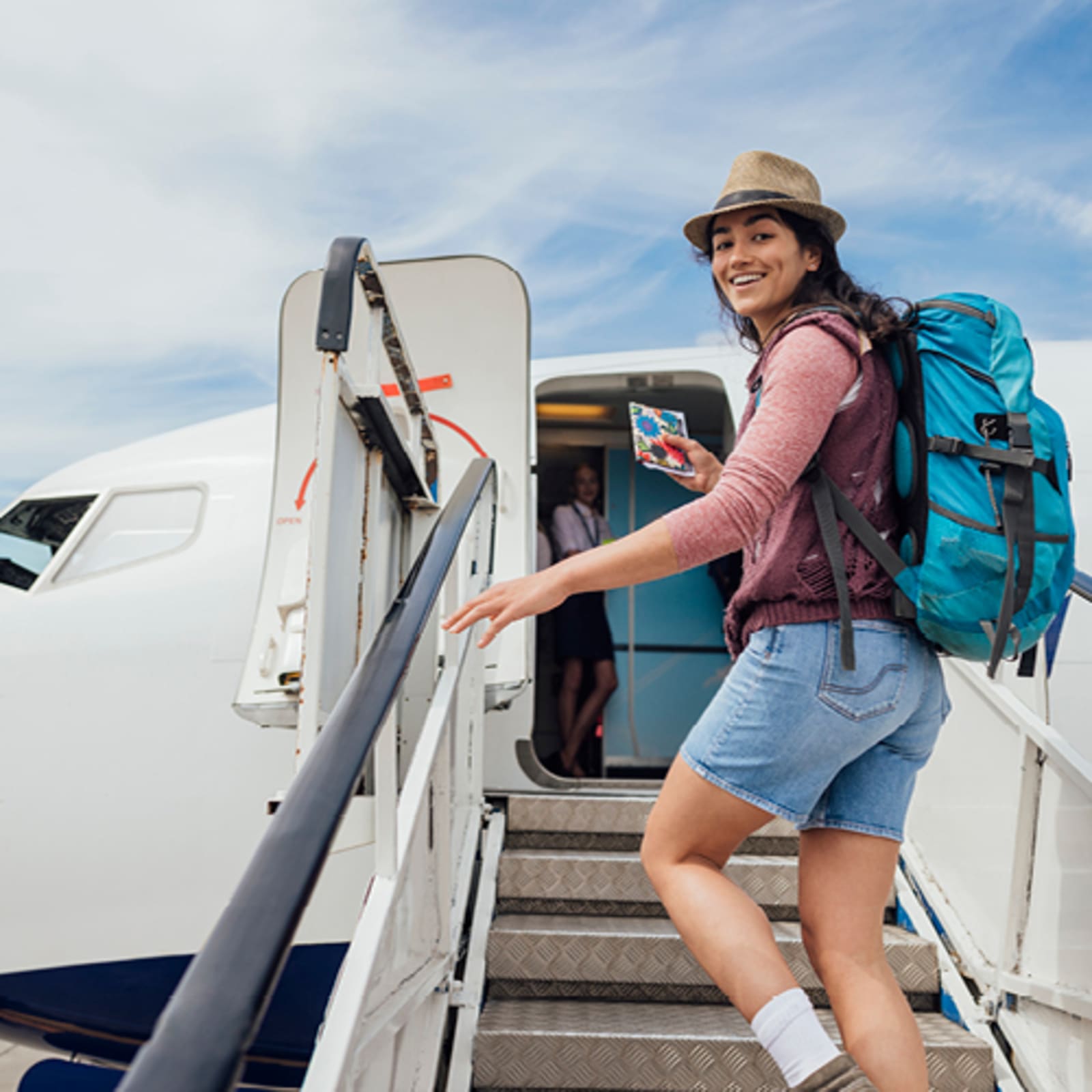 Woman smiling wearing a blue backpack, walking up the steps to board a plane