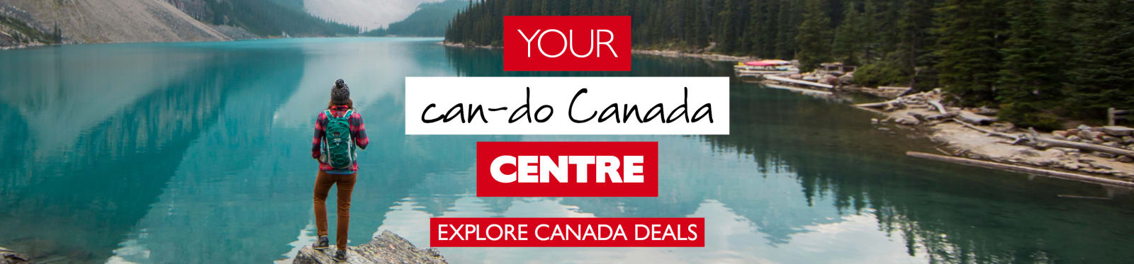 Your can-do Canada centre - explore Canada deals. Hiker standing on a rock looking out at a calm lake with mountains and pine trees in the distance