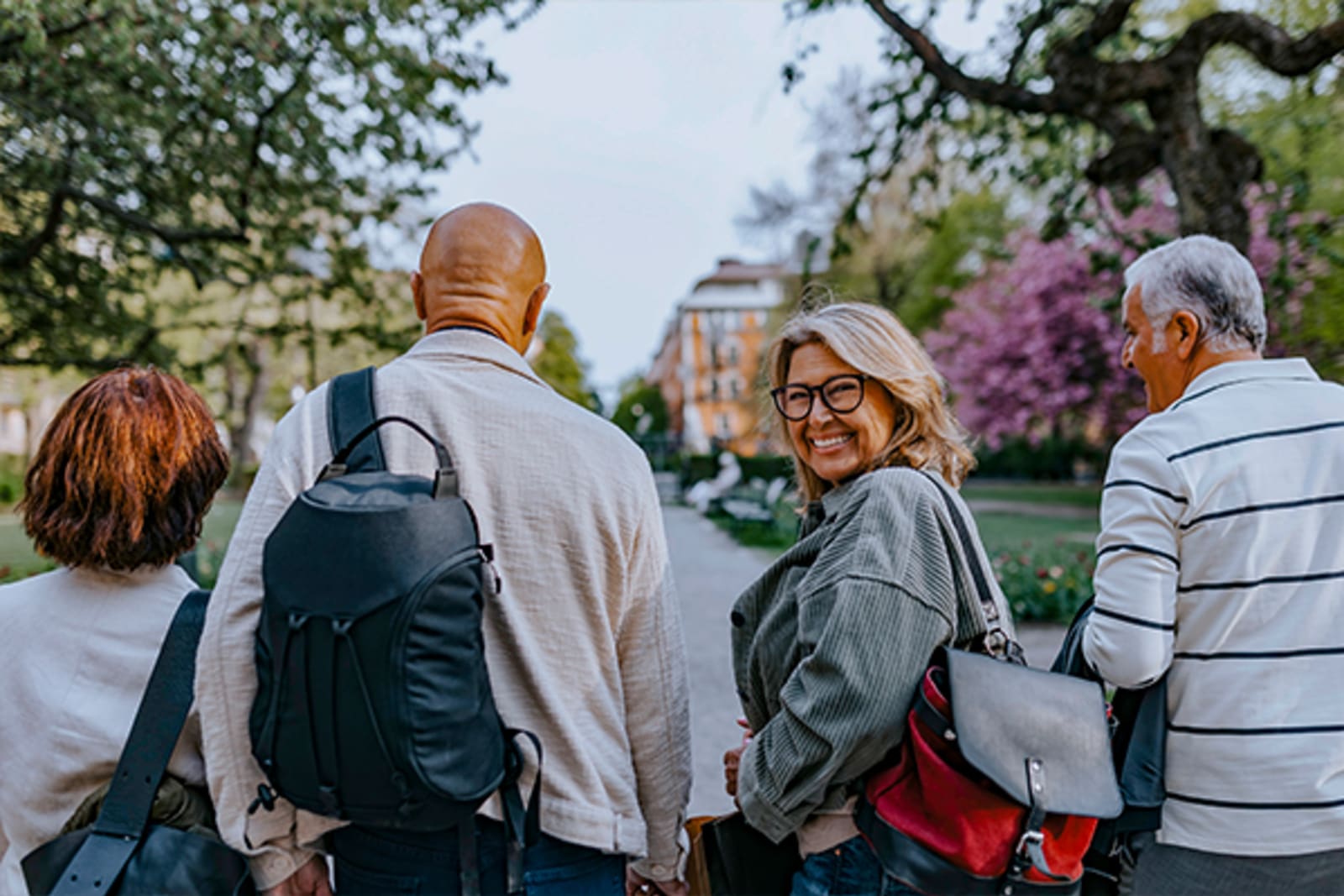 Woman looking back at the camera smiling as her group walks down a tree-lined path