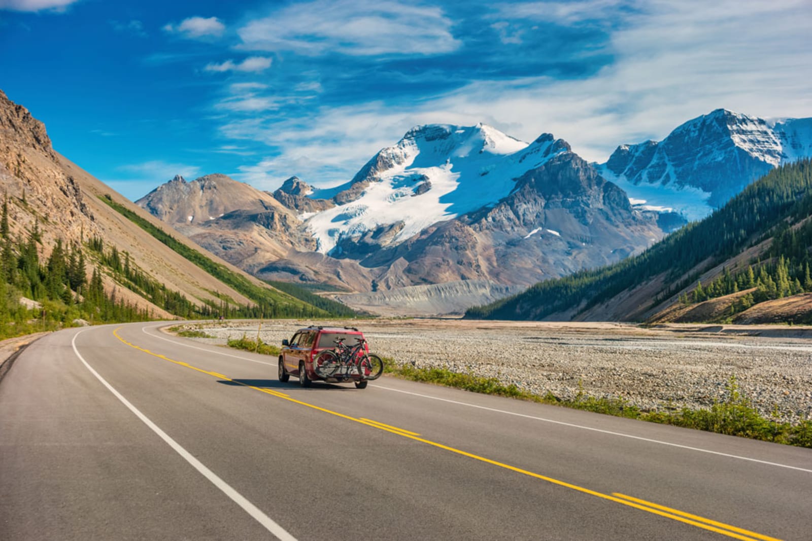 SUV with bicycle rack and bicycles travels along the Icefields Parkway in the Canadian Rockies, Alberta, Canada on a sunny afternoon. Mt Athabasca is in the background.
