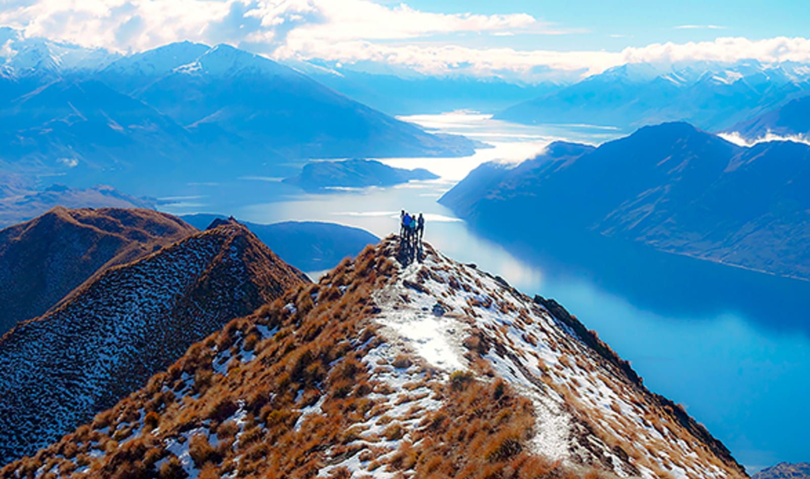 people standing on top of a mountain with lake at the base in queenstown