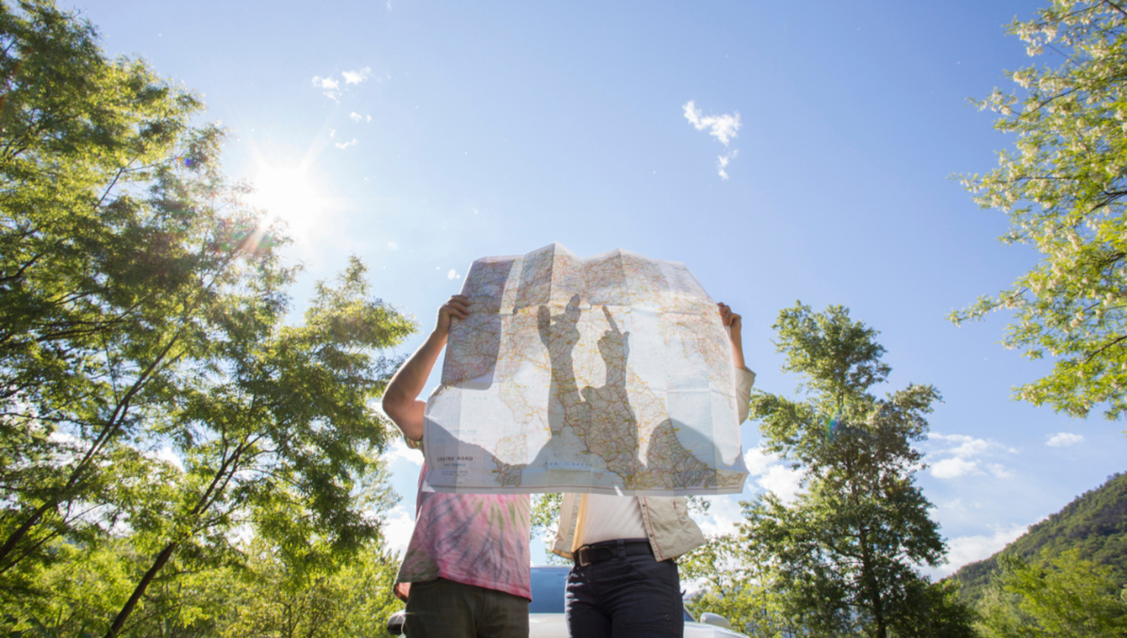 The shadow of two people showing through a paper map of Italy as they analyse it and point 