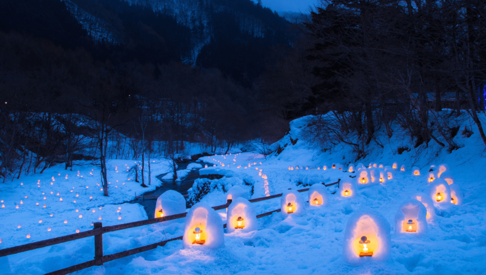 Small lanterns covered in small huts made out of snow lining a river