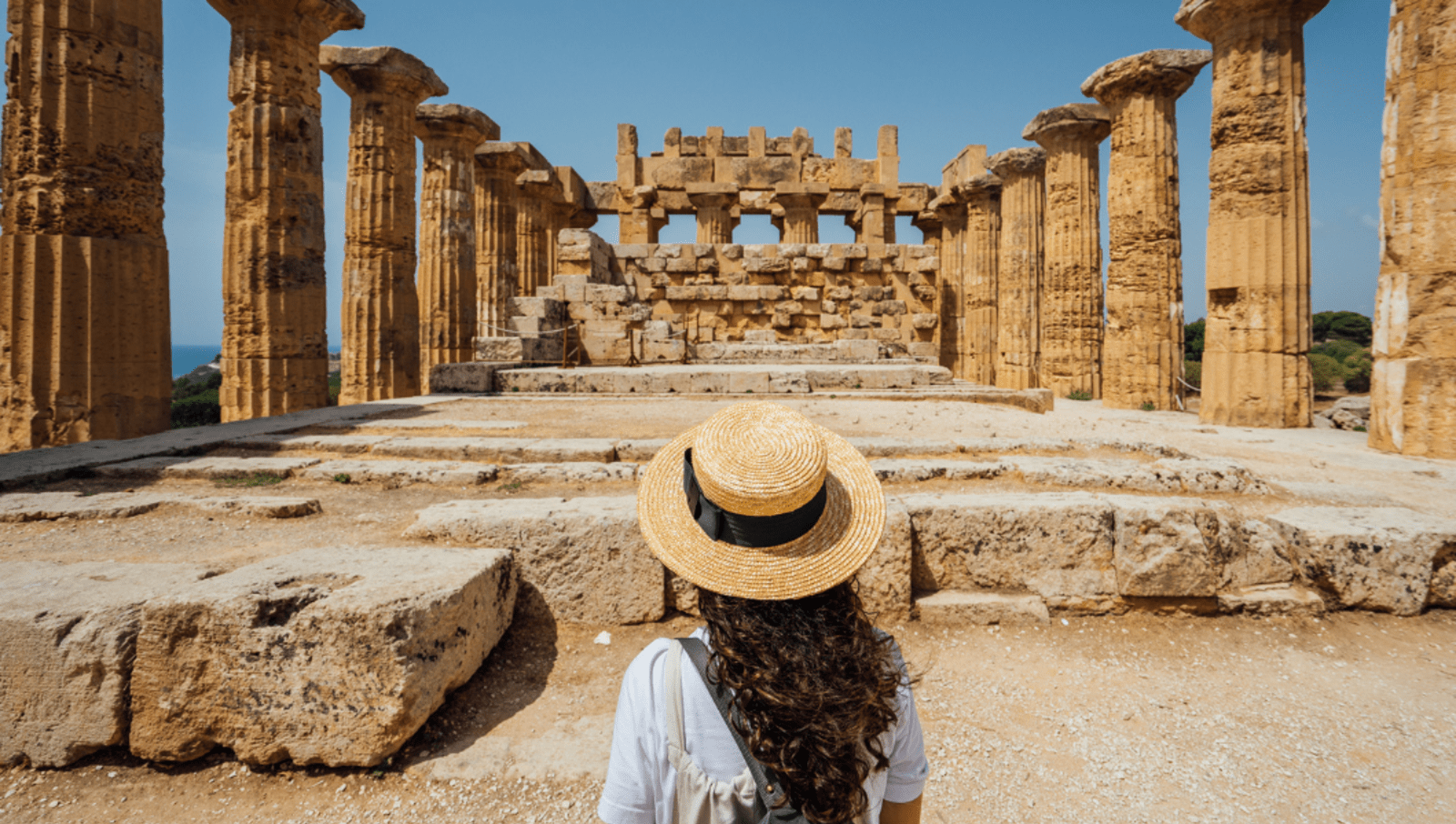 Woman with a straw hat looking at the ruins of an ancient temple in Sicily