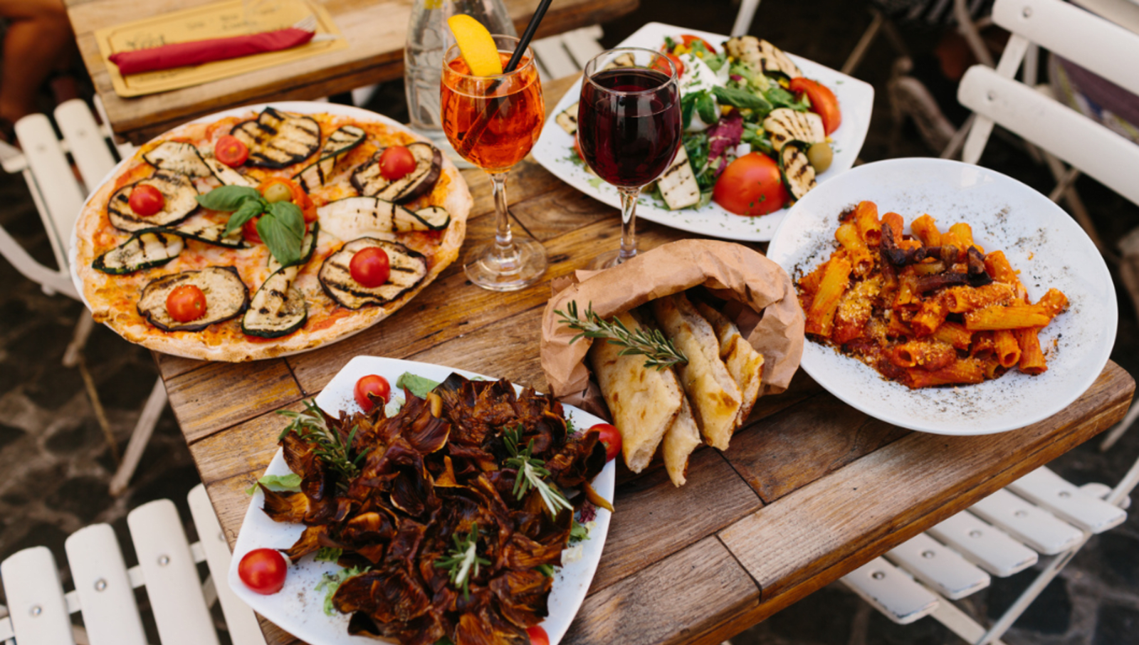 Pasta, salad, pizza and glasses of wine laid out on a table at a restaurant in Italy