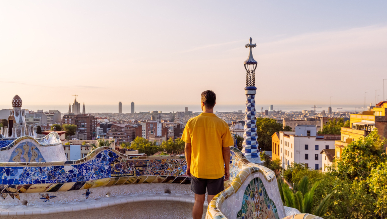 Man in yellow shirt looking out to barcelona city while standing at a lookout with mosaic artwork