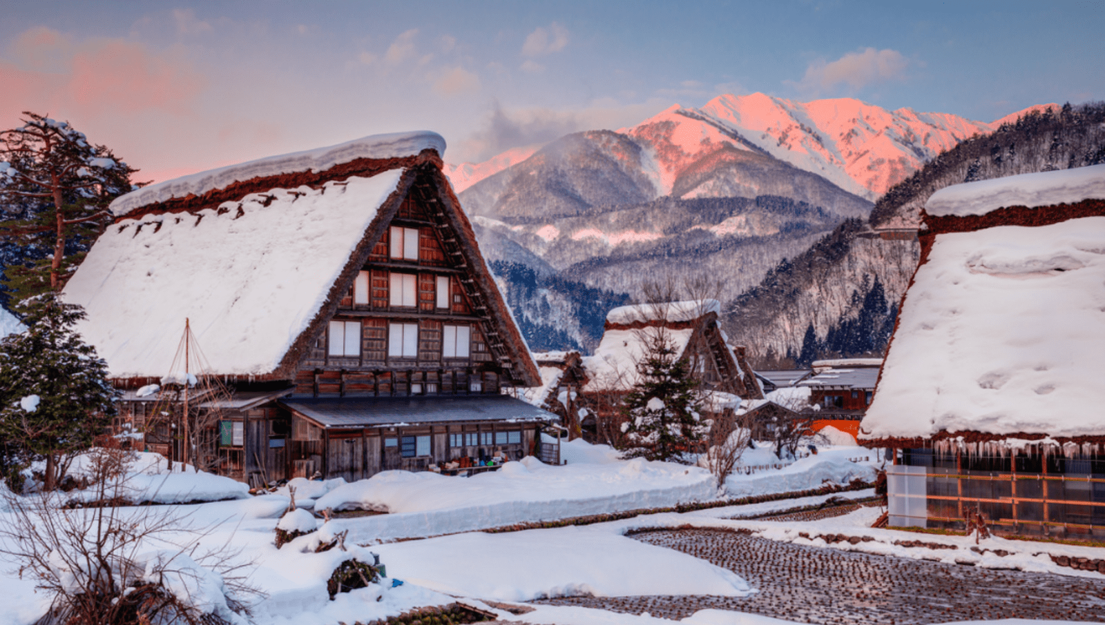 Large wooden huts with snow on their roof in a small town underneath mountains at sunrise