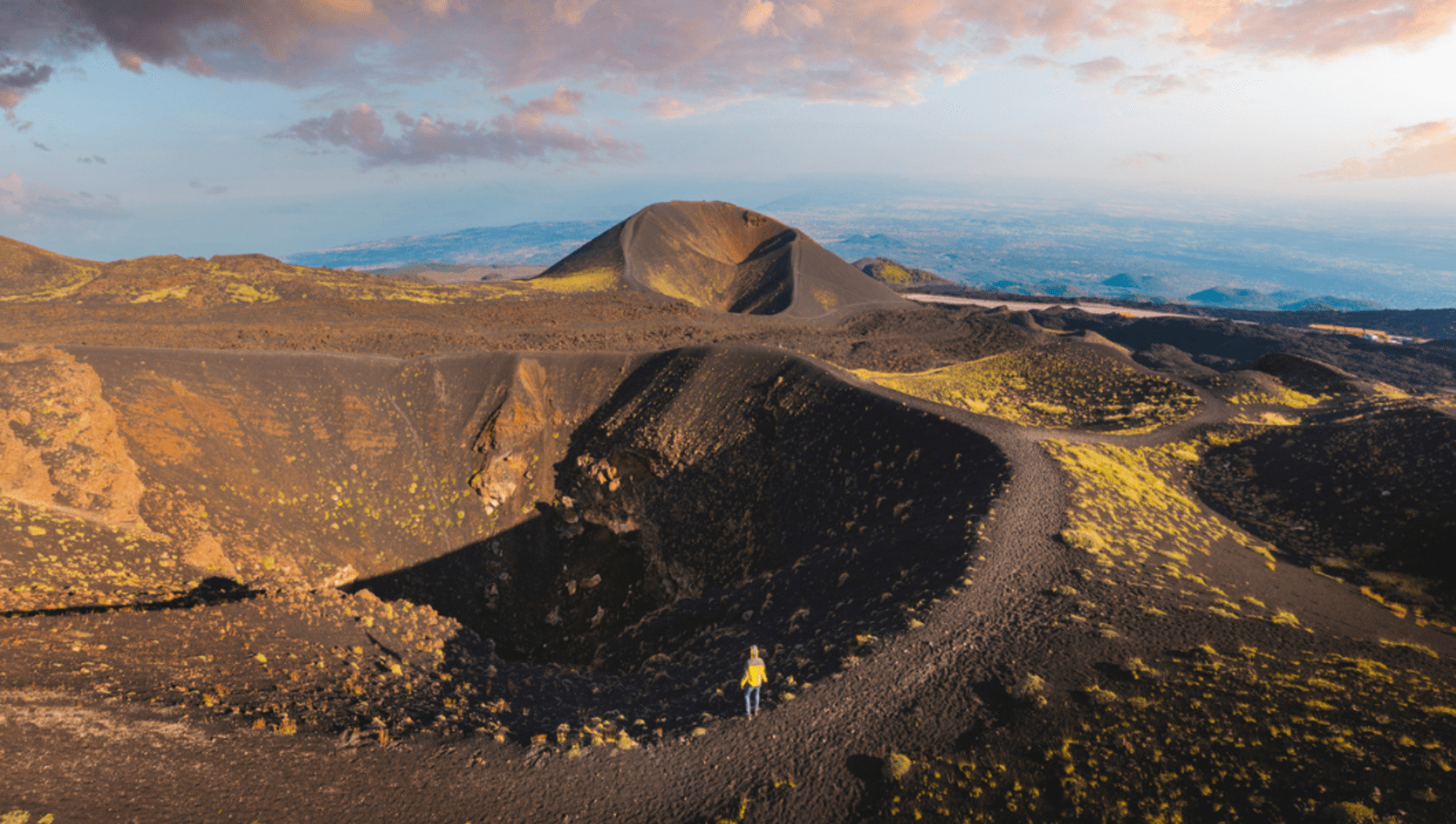 Person standing on the edge of a volcanic crater at Mount Etna 