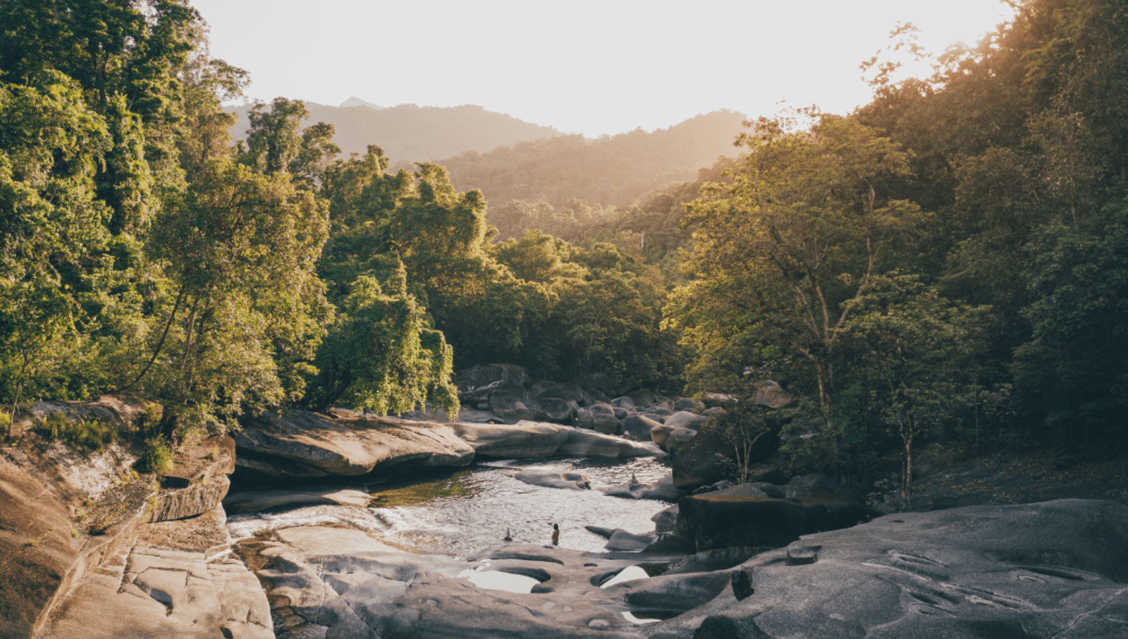 Person standing in a small pool surrounded by boulders and trees