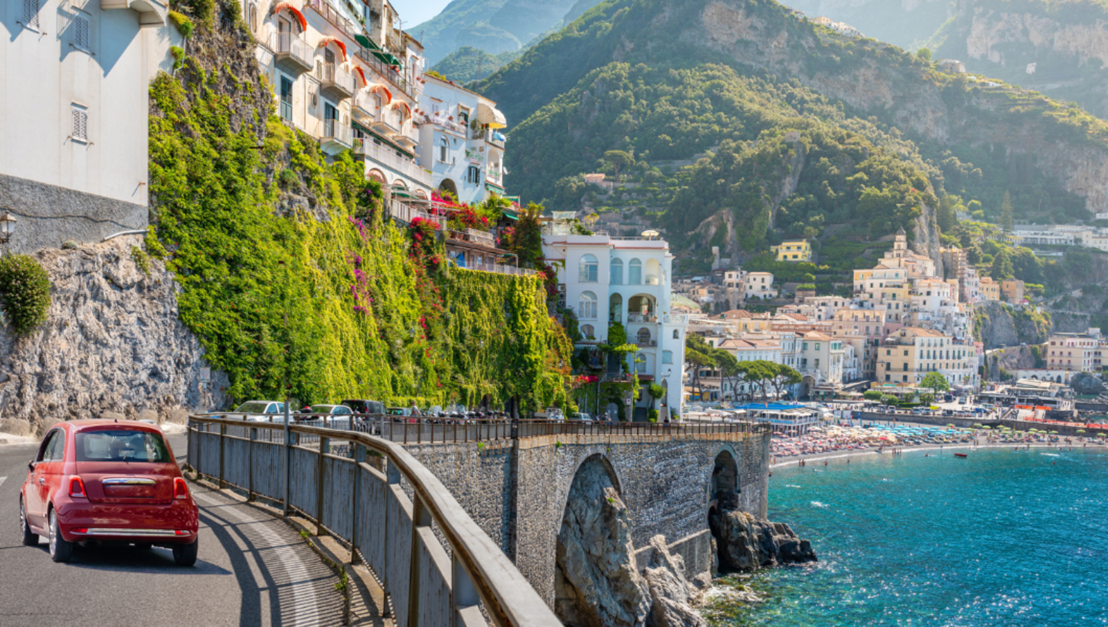 Small red car driving on road on the edge of a cliff on the Italian coast