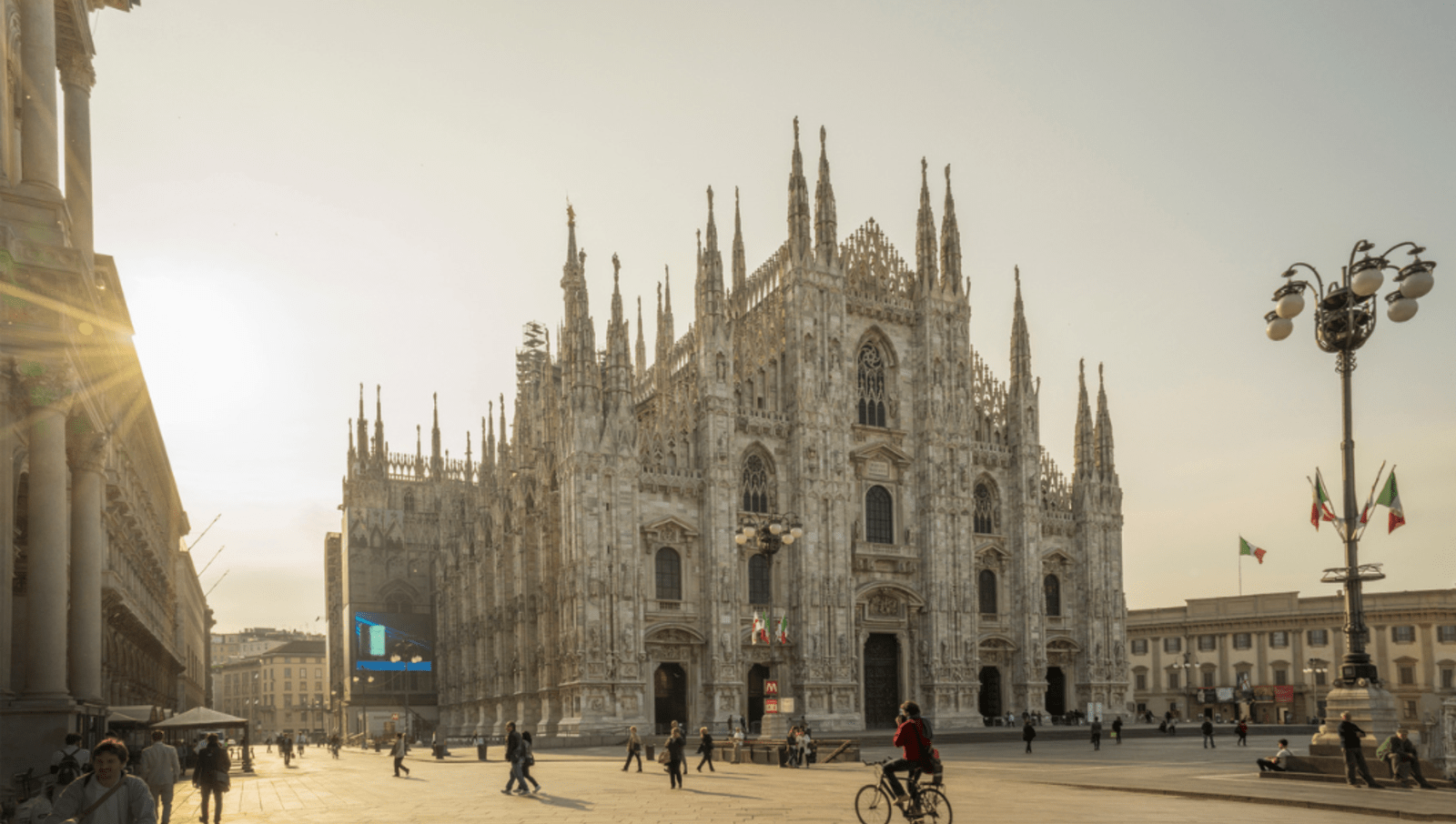 Large cathedral in a square with sun shining behind in Milan