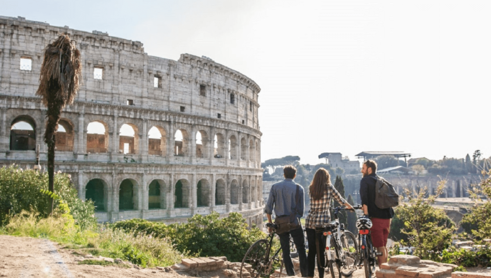 Three friends with bikes standing on a hill looking at the Colosseum 