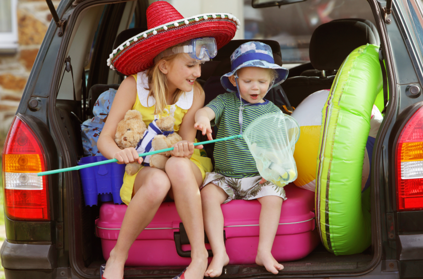 Two young children sitting in the back of a car packed up for a holiday