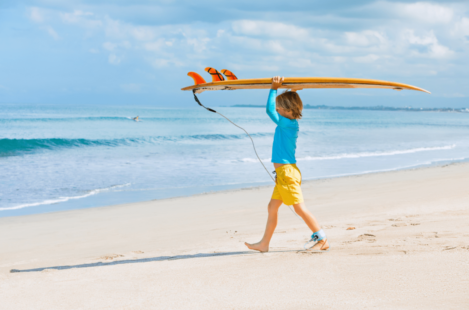 Young boy on a beach carrying a surf board into the ocean