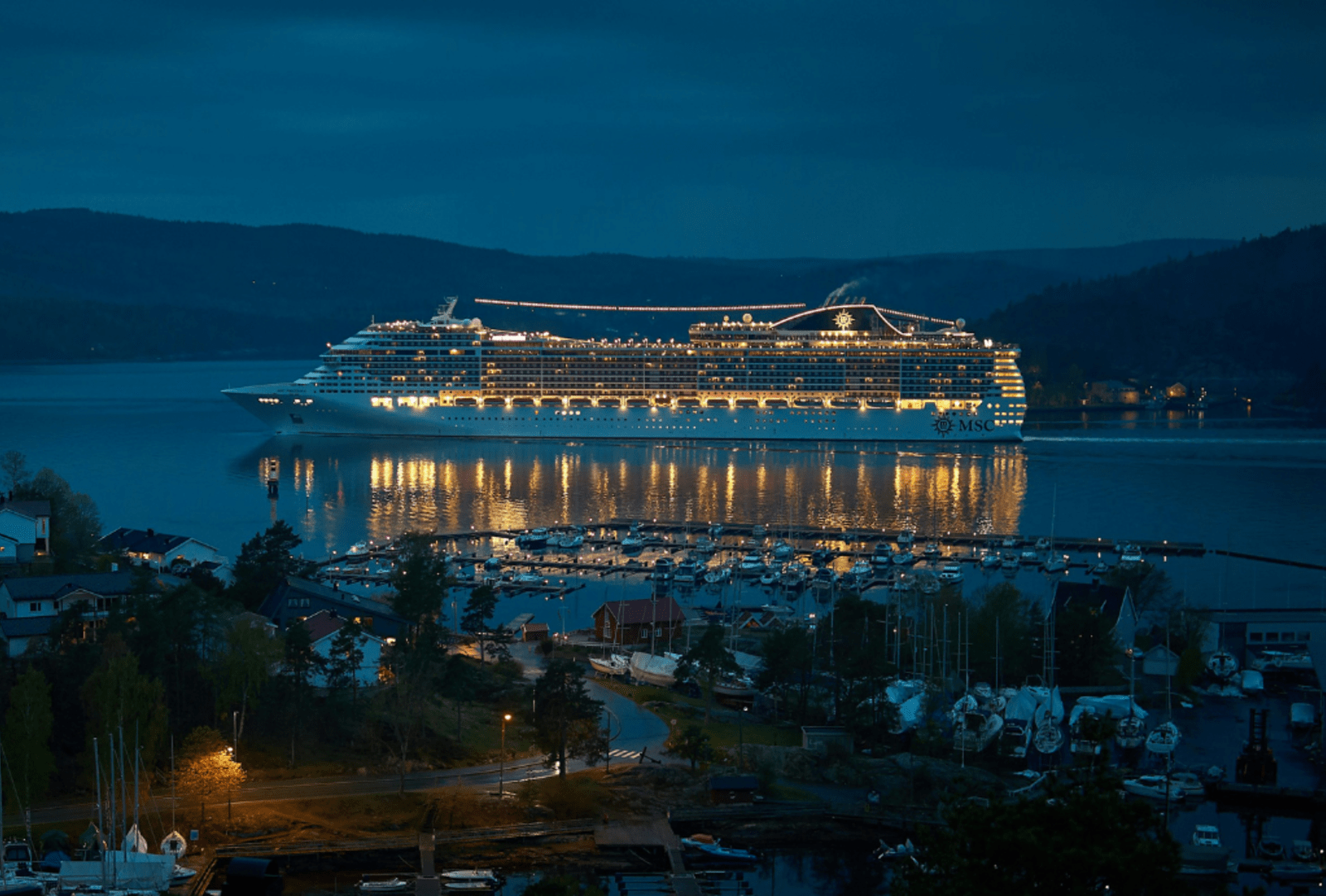 A cruise liner sails into a hilly harbour at night.