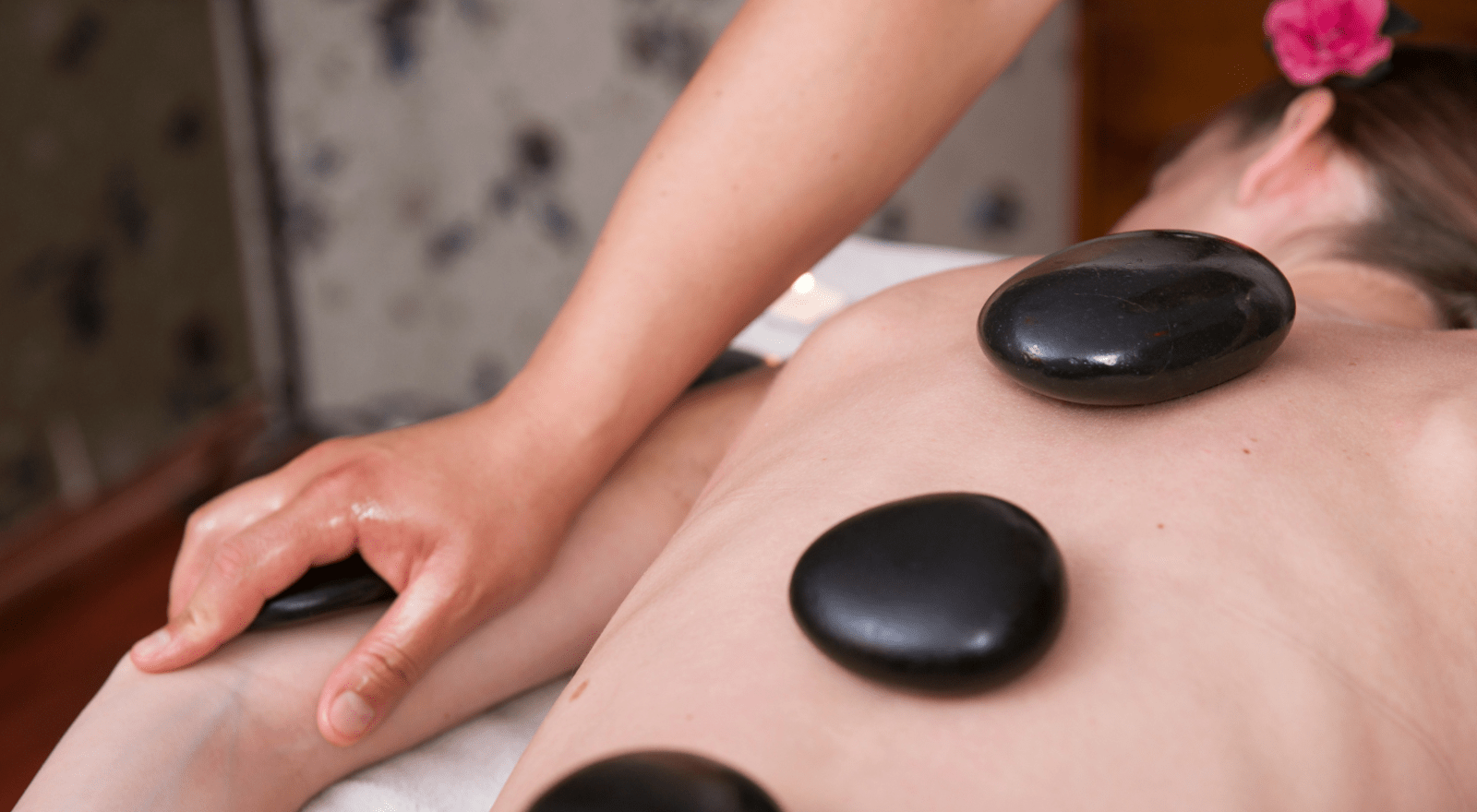 A woman lies face down with massage stones placed on her back
