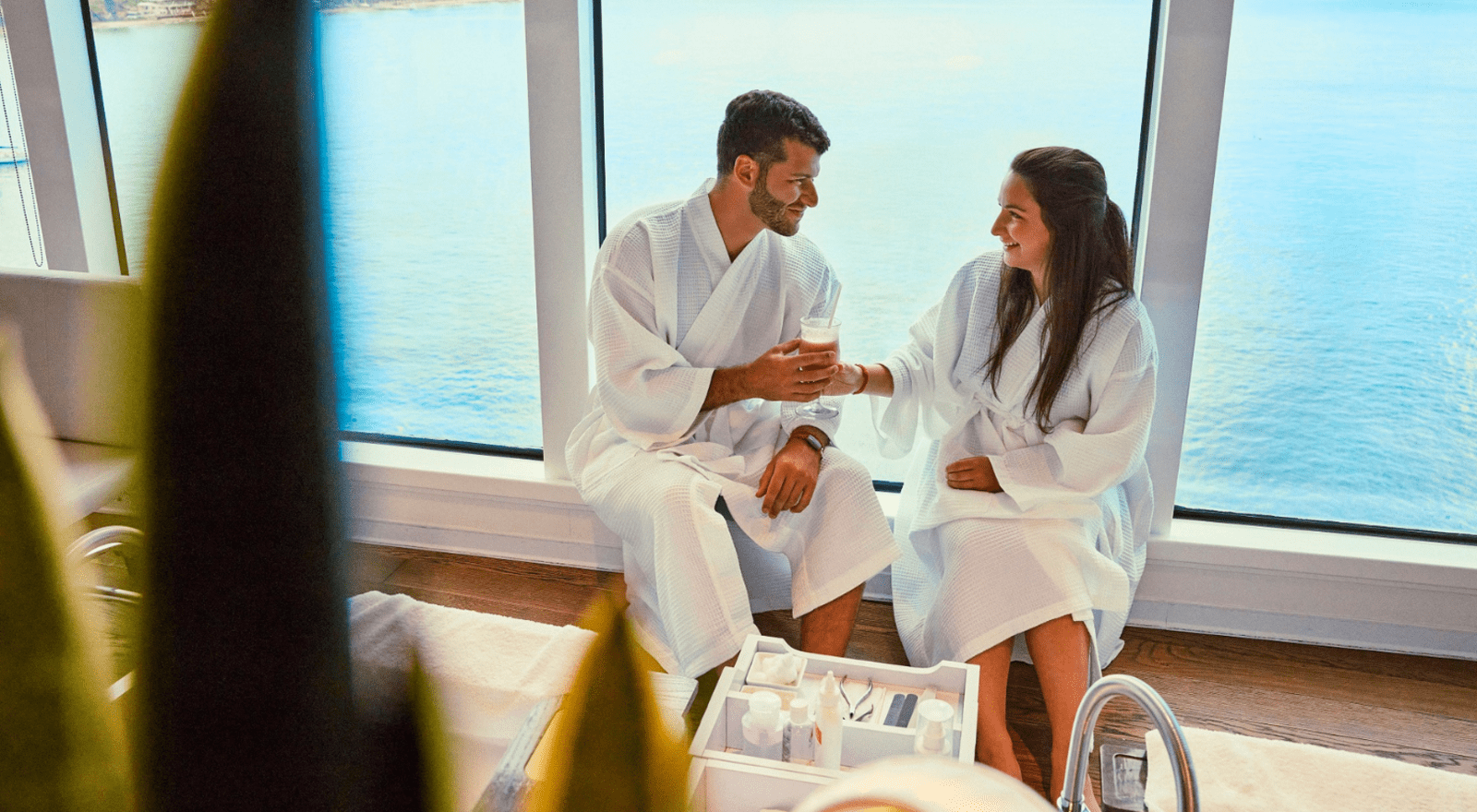 A couple in bathrobes share a drink inside a cruise ship