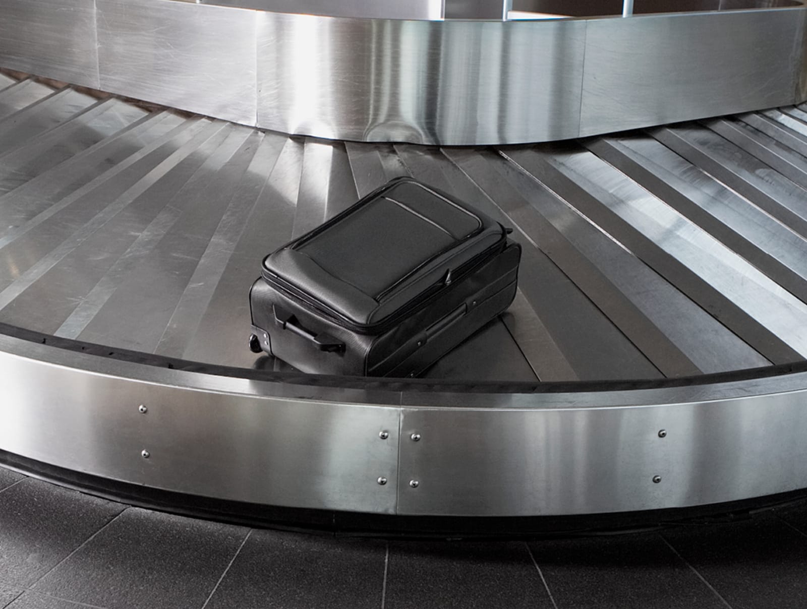 Black luggage bag sitting alone and unattended on a baggage carousel at the airport