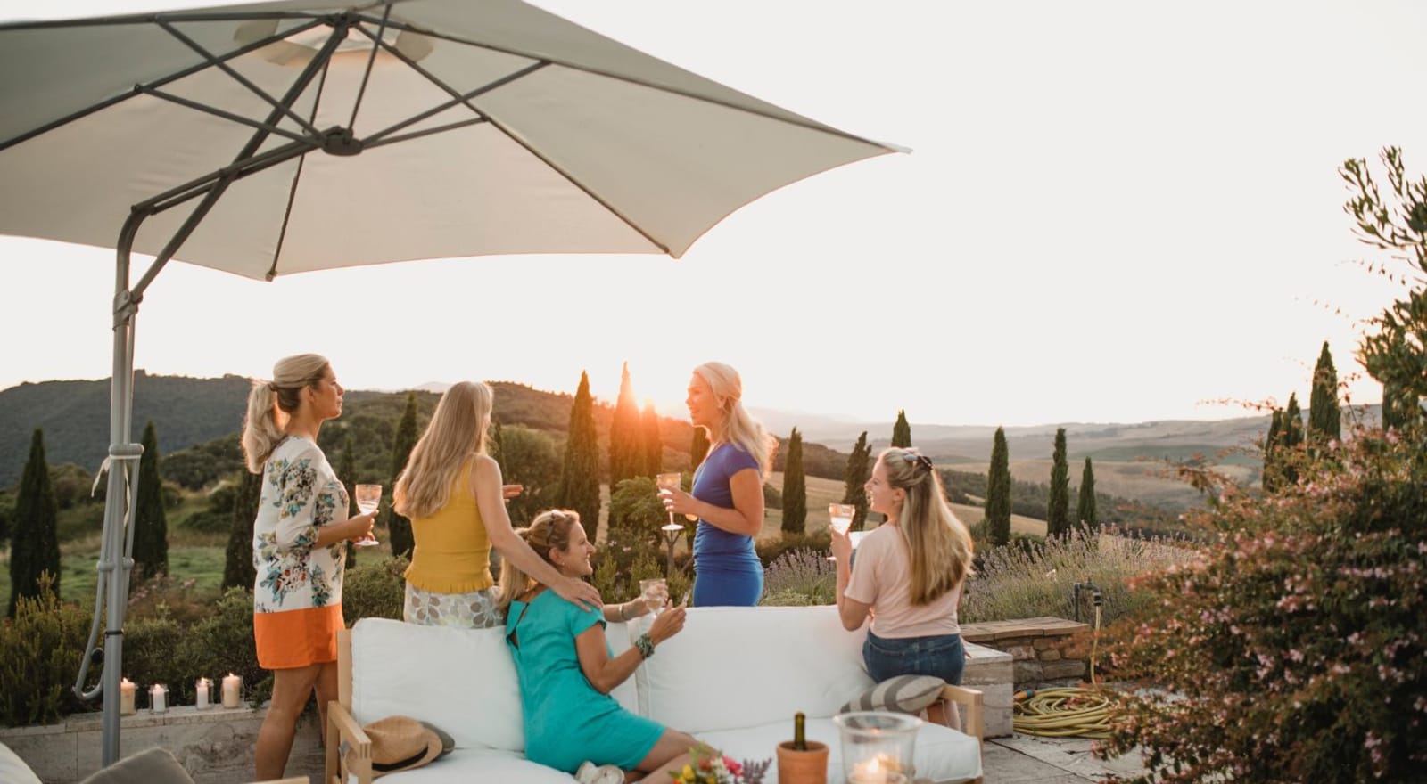 group of women sitting on couch and standing while holding wine and watching the sunset