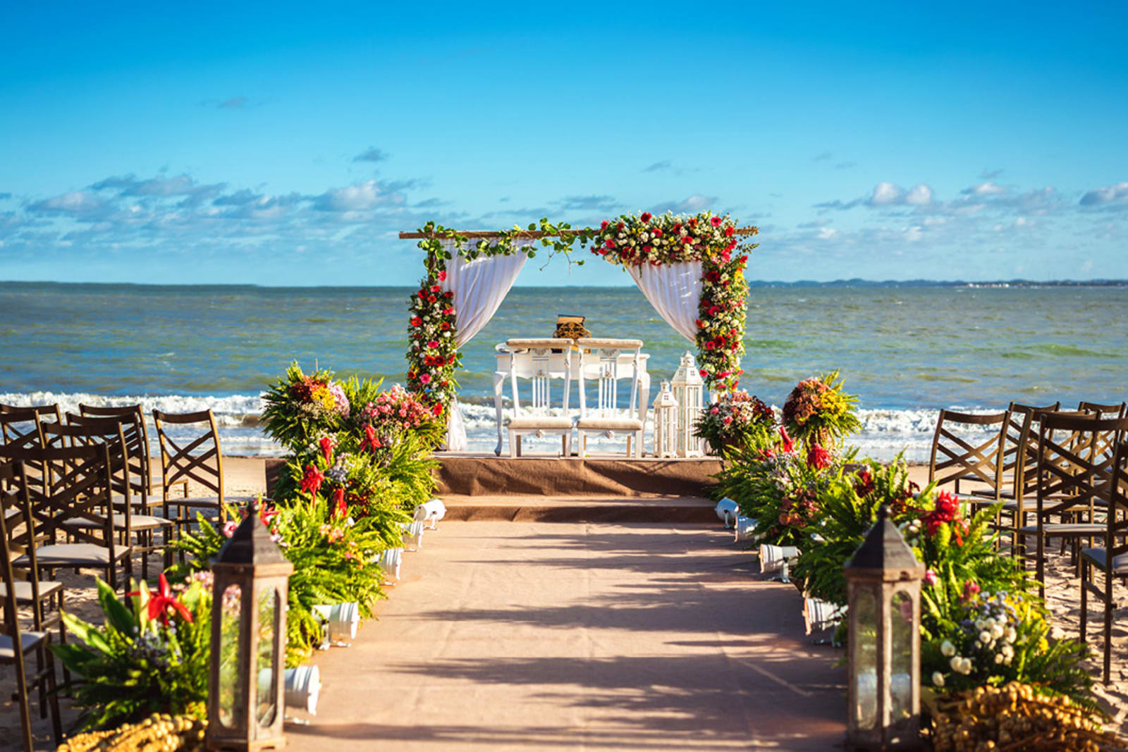 An altar, chairs, flowers and other destination wedding decor set up on the beach