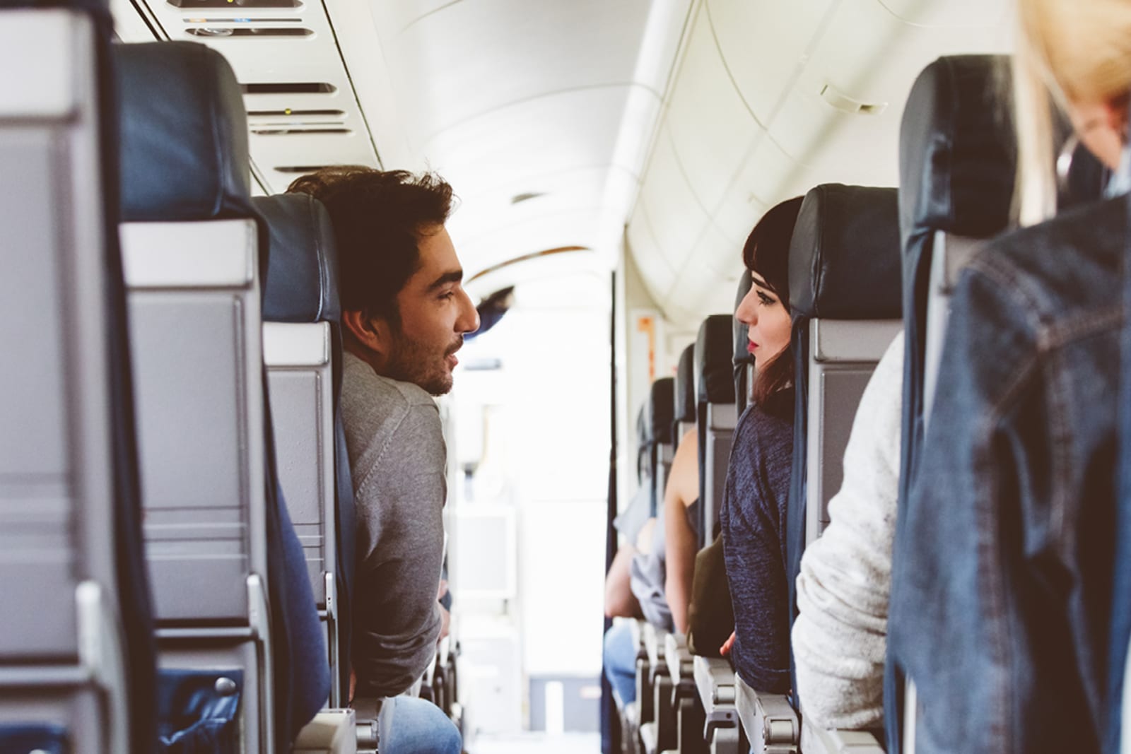 Two passengers on an airplane, speaking to each other across the aisle
