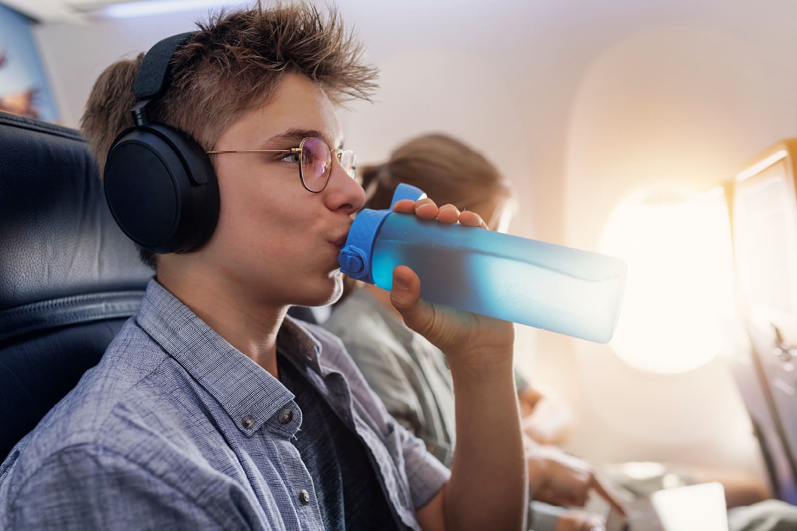 Person drinking from a reusable water bottle while on a flight