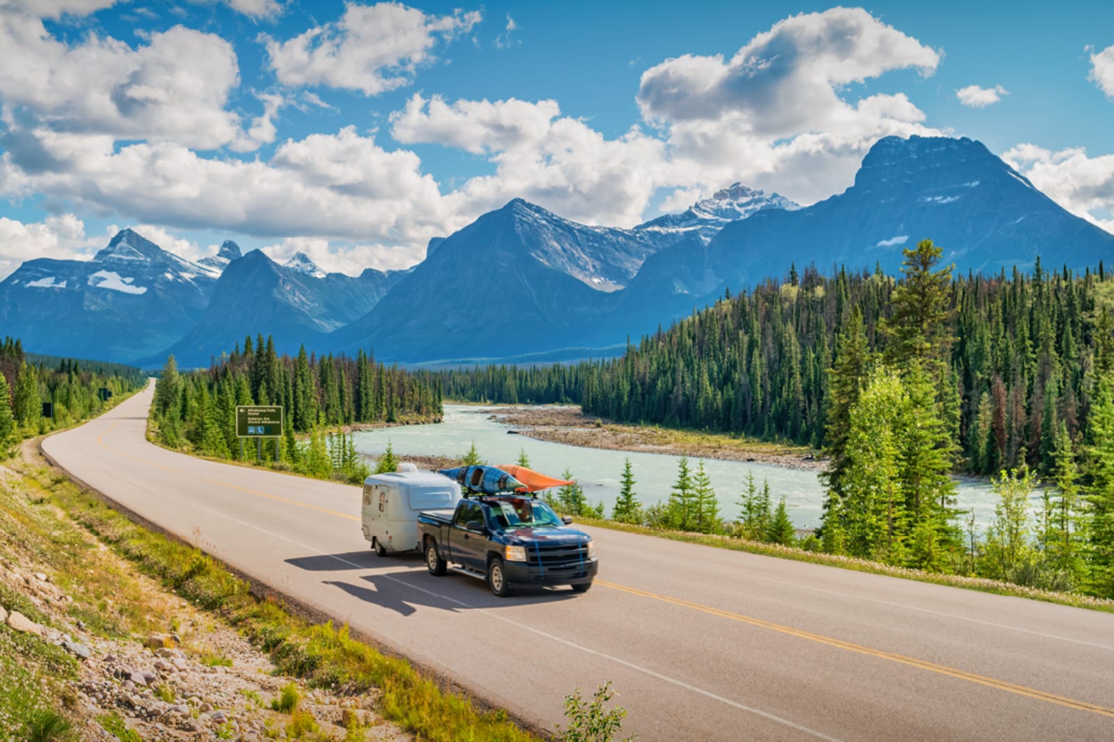 A truck with a trailer and two kayaks driving down a stretch of the Icefields Parkway in Alberta
