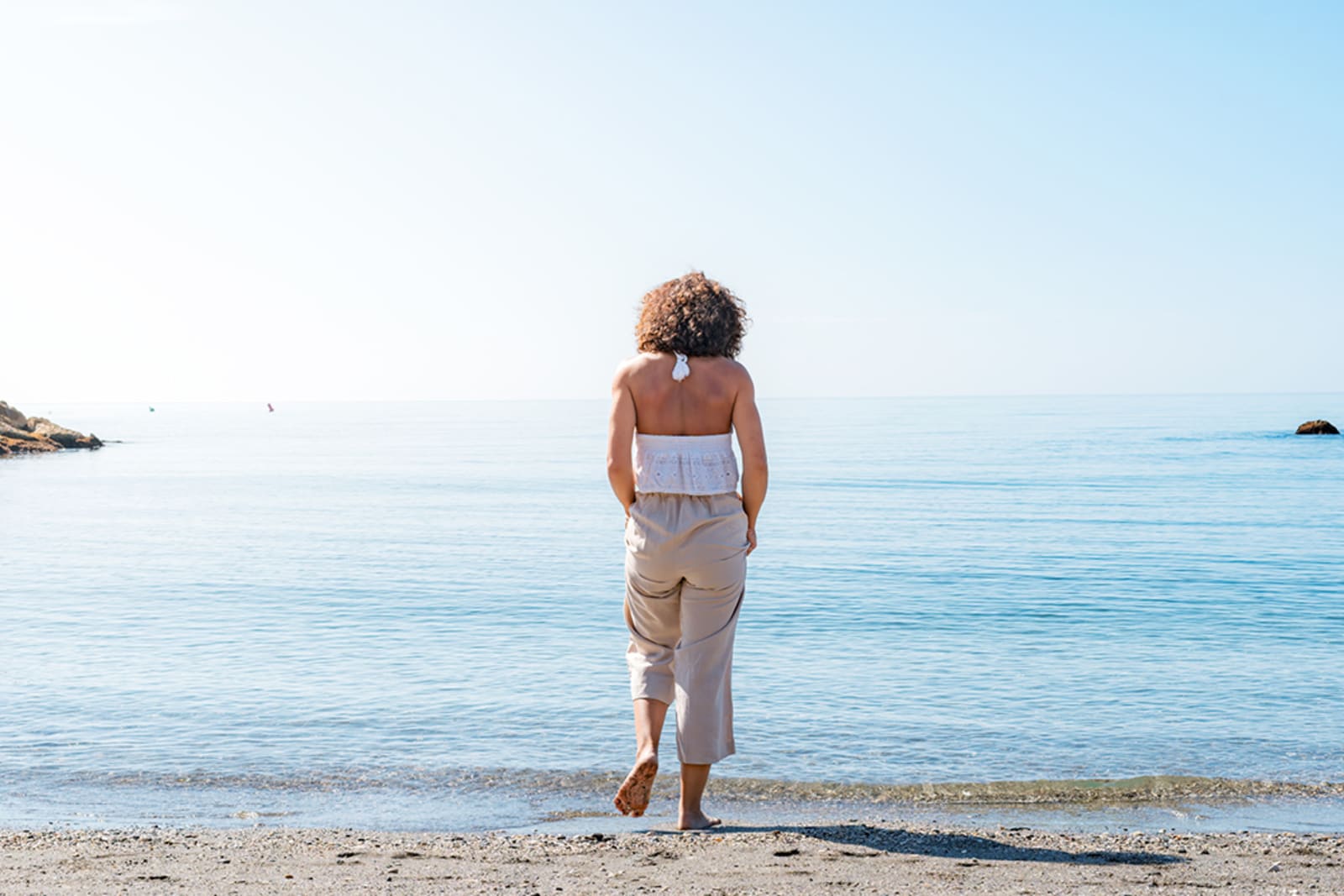A woman standing on a beach; she's wearing a neutral outfit from the capsule wardrobe she packed