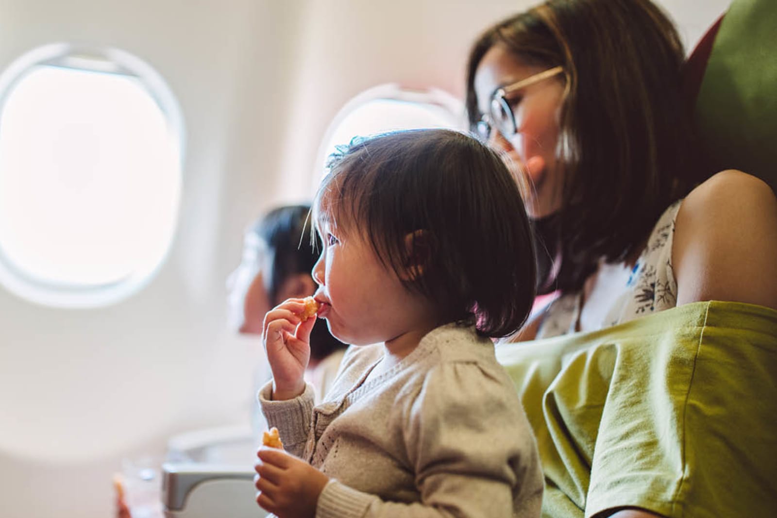 A mother and her young children on a plane; one of the children sits in her lap