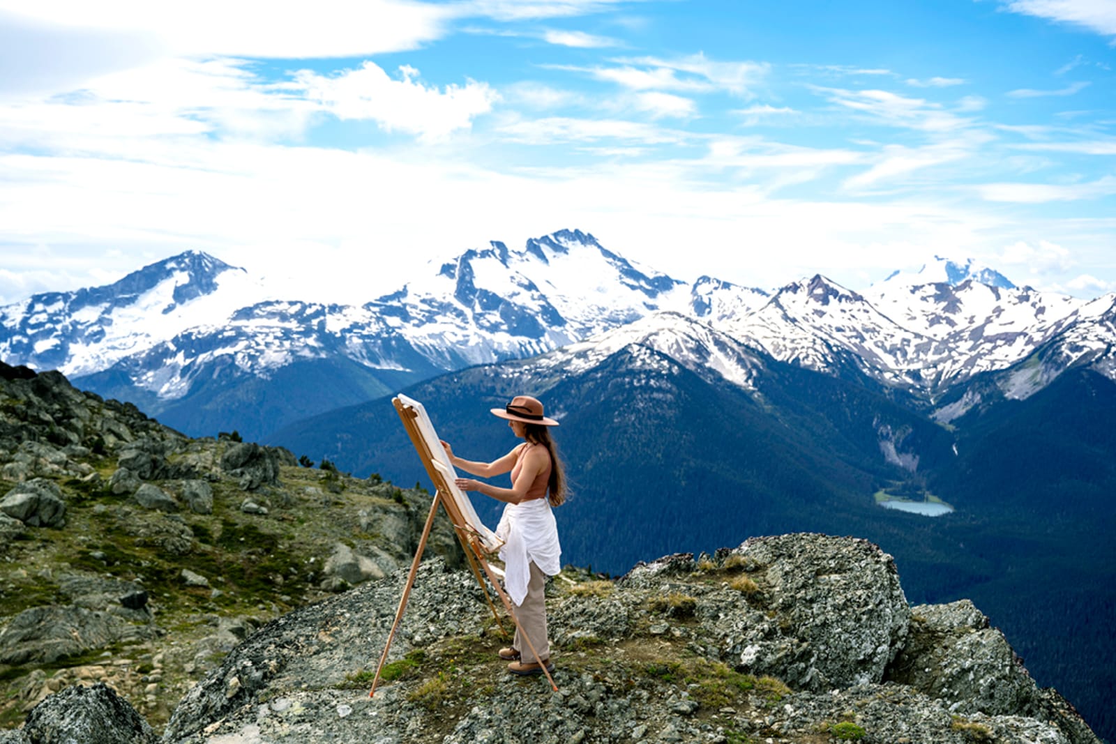 A traveller embracing the concept of slow travel by painting at the top of a mountain