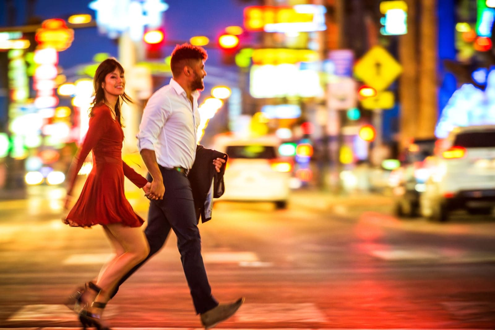 A couple walking on the Las Vegas Strip at night; she's wearing a long-sleeved dress and he's carrying a lightweight jacket