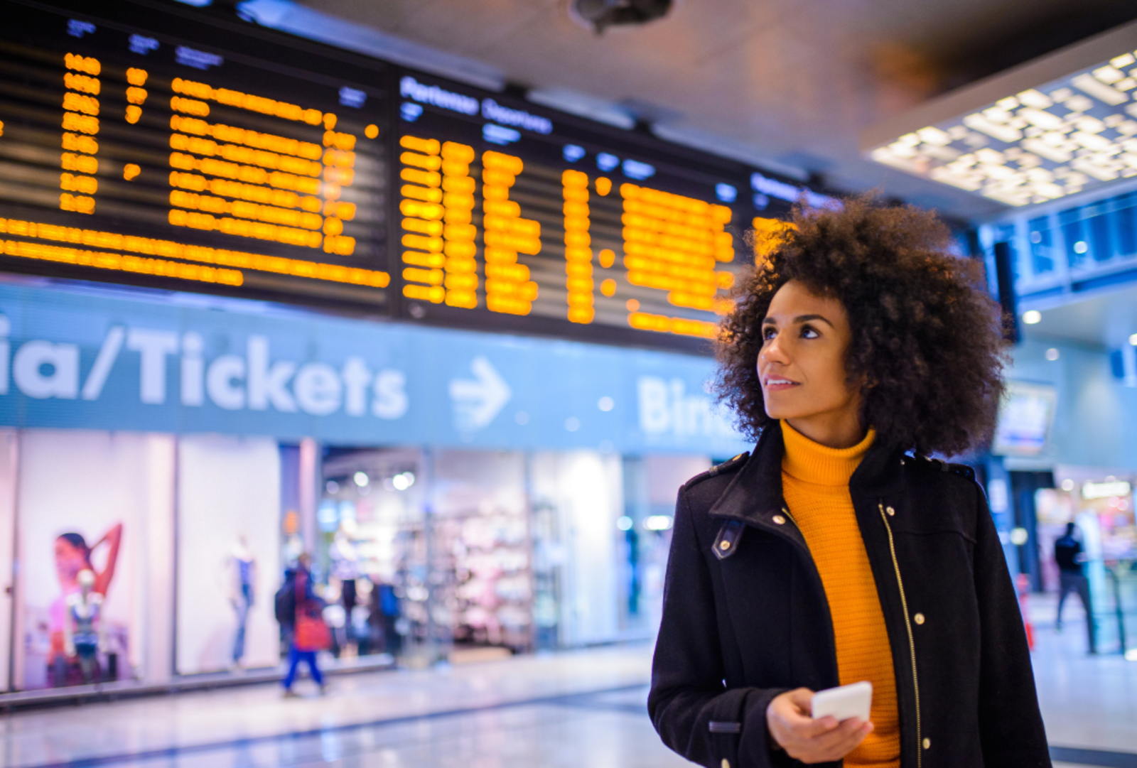A person checks an overhead digital flight schedule at an airport terminal