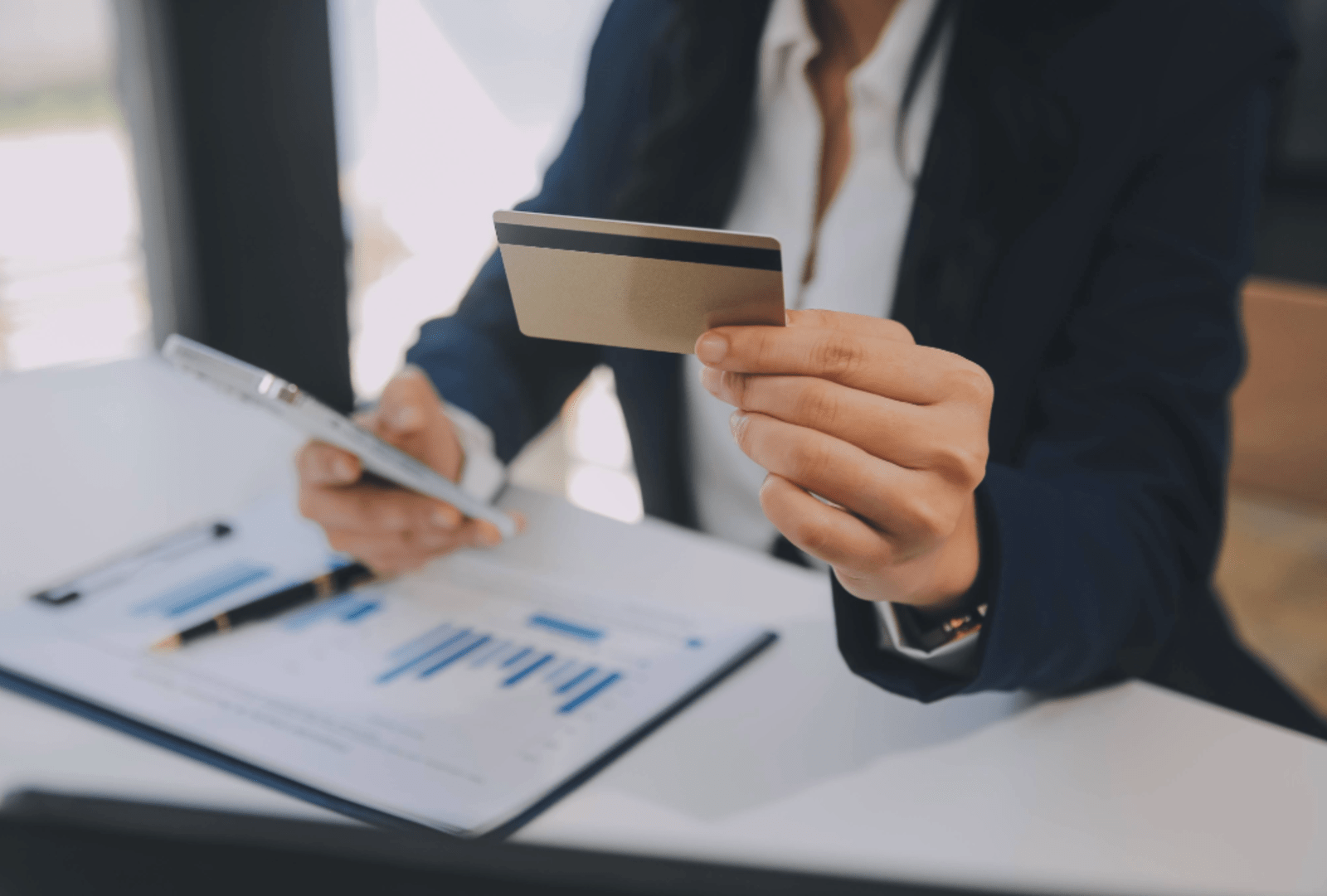 A woman works out finances holding a credit card and an iphone