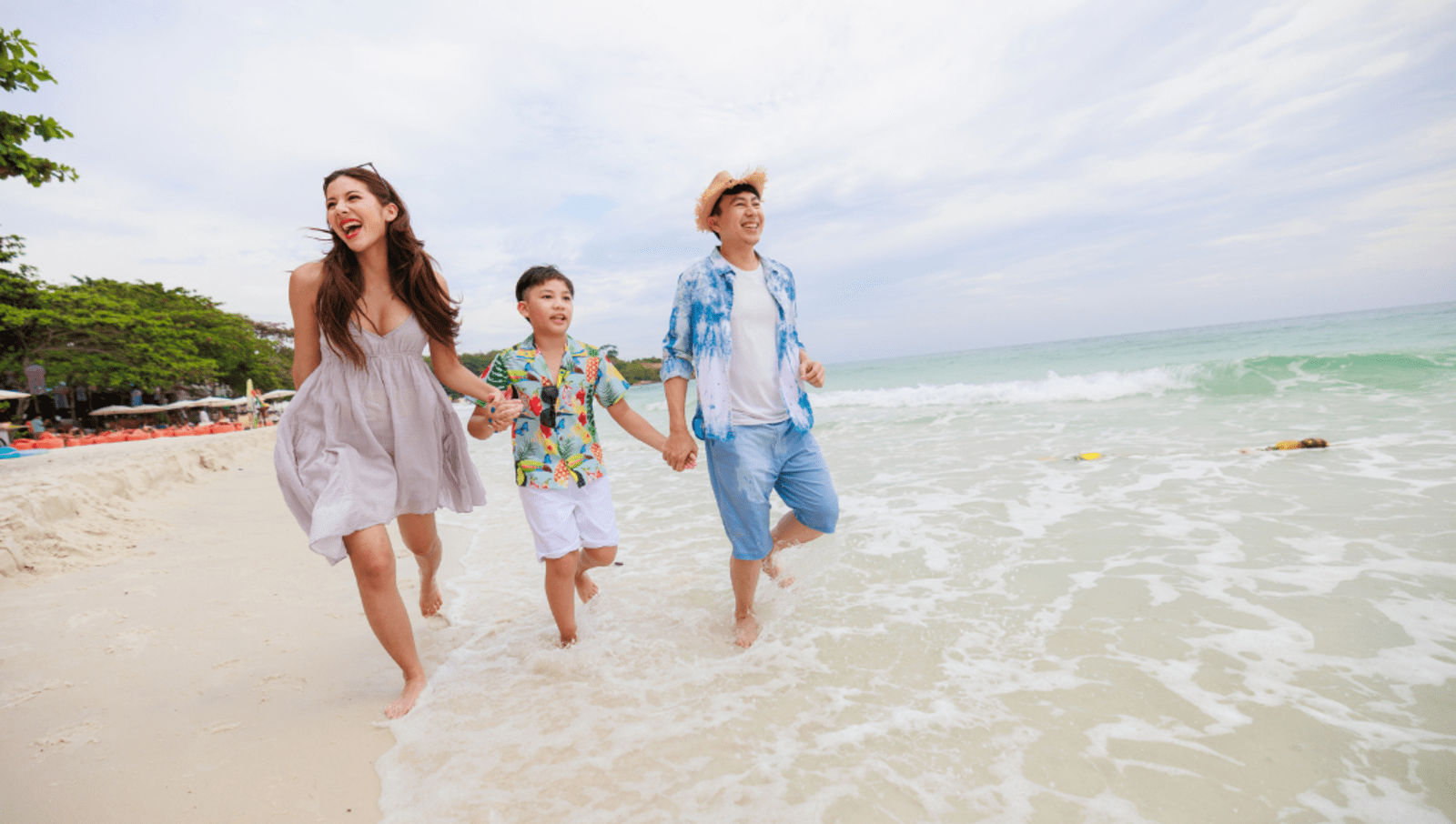 Two adults and a child run in the water at a beach in Thailand 