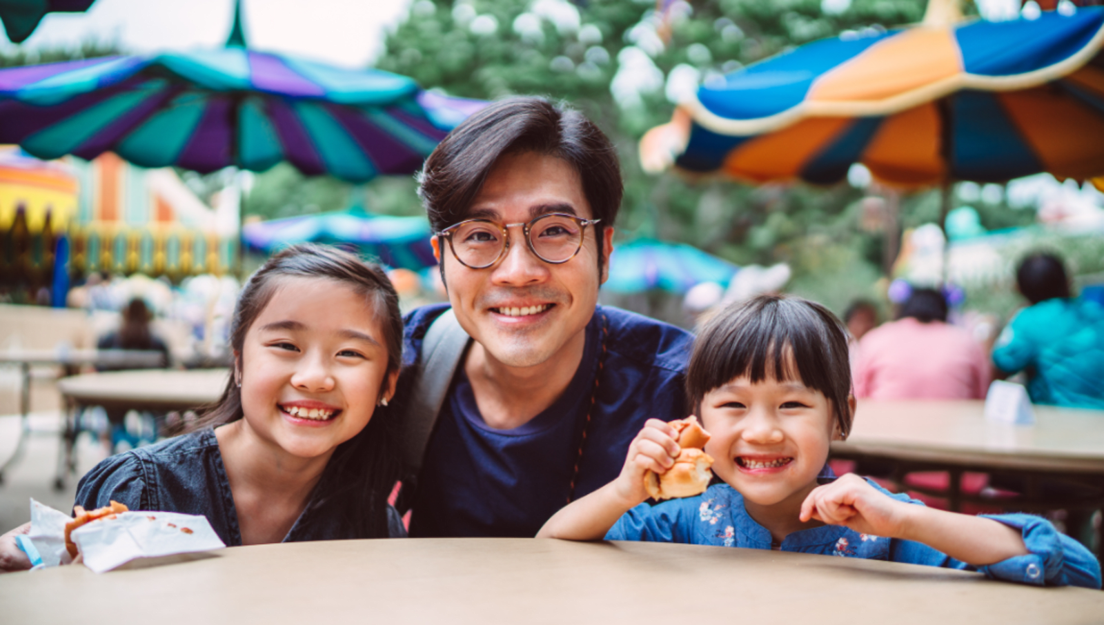 Adult and two children sit at a table in an amusement park in Hong Kong 
